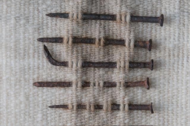 Detail of Handwoven wool, walnut wood and rusty nails wall hanging sculpture with long brown shaded fringe on a white wall