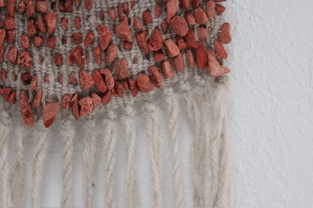 A detail of Red Coral & Wool Adornment hanging on a small oak frame on a white wall