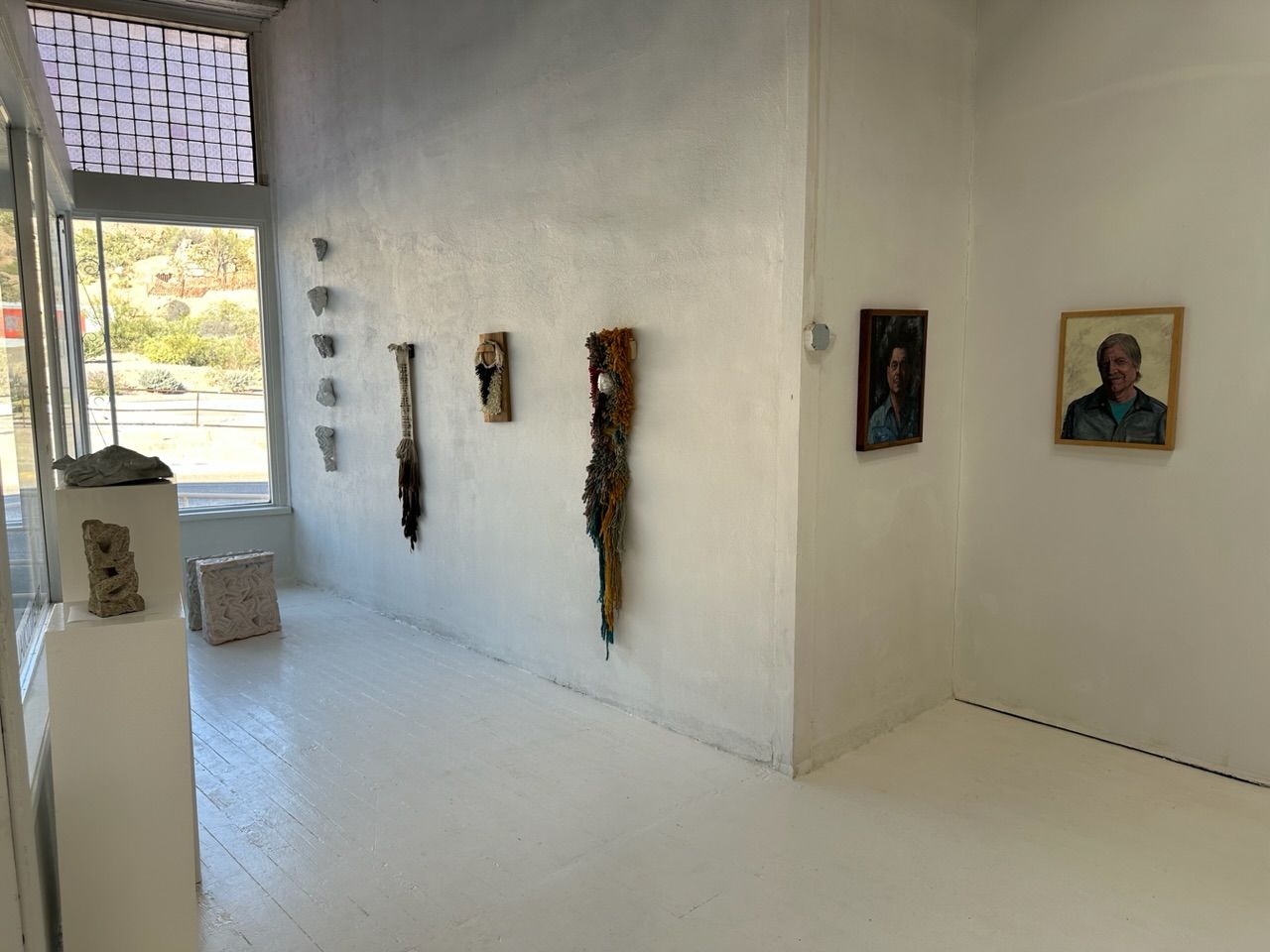 A handwoven sculptural necklace of black coral and mother of pearl hanging on a wooden frame On a white wall