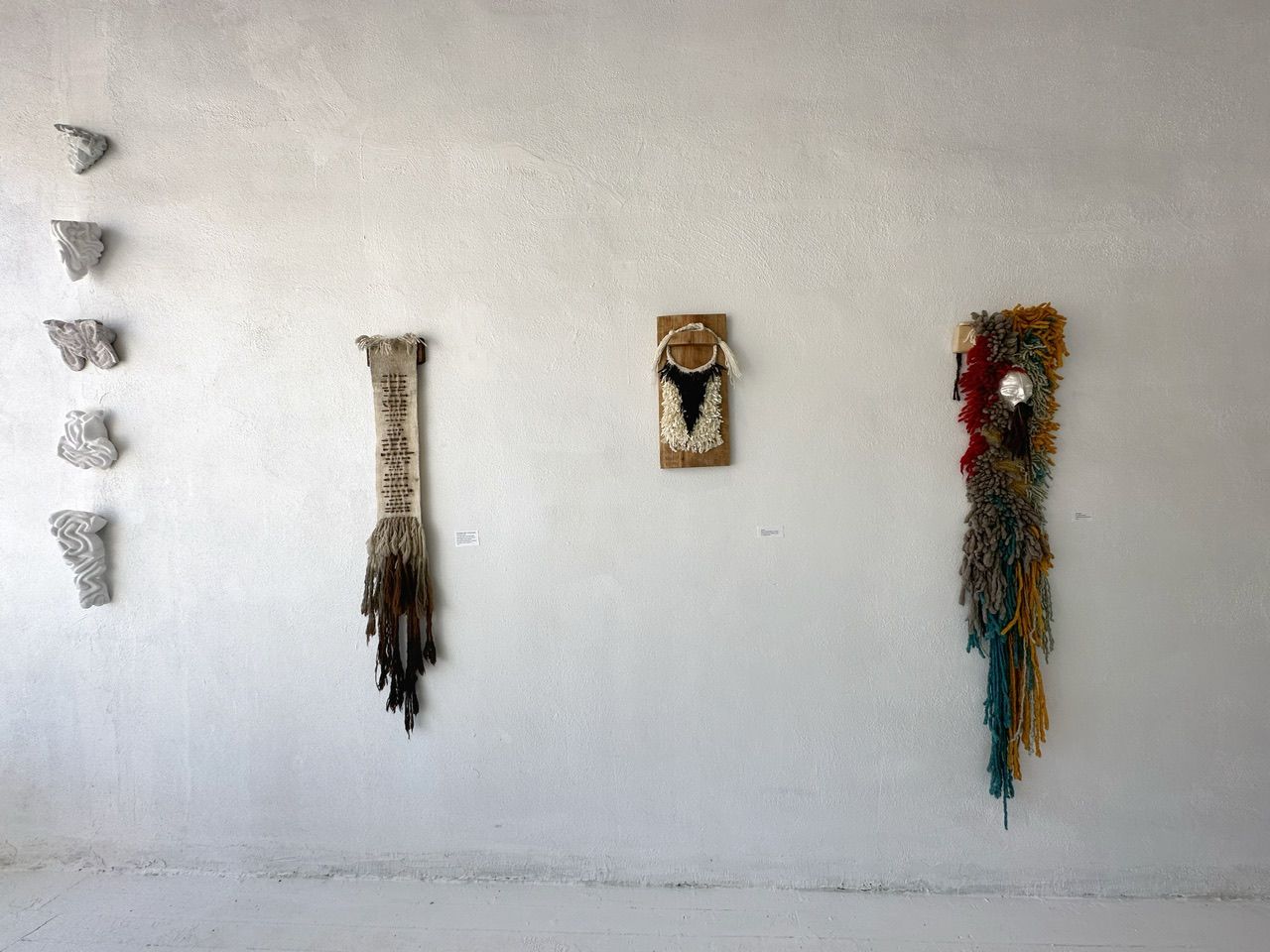 A handwoven sculptural necklace of black coral and mother of pearl hanging on a wooden frame On a white wall