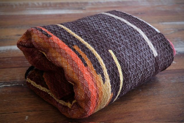 Handwoven diamond pattern organic cotton linen fabric in rich shades of fall and earth, brown, red, orange, yellow and a little green, folded on a wooden floor
