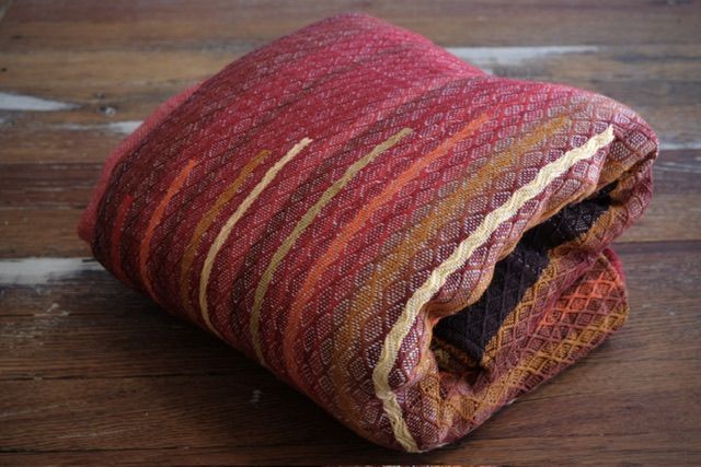 Handwoven diamond pattern organic cotton linen fabric in rich shades of fall and earth, brown, red, orange, yellow and a little green, folded on a wooden floor