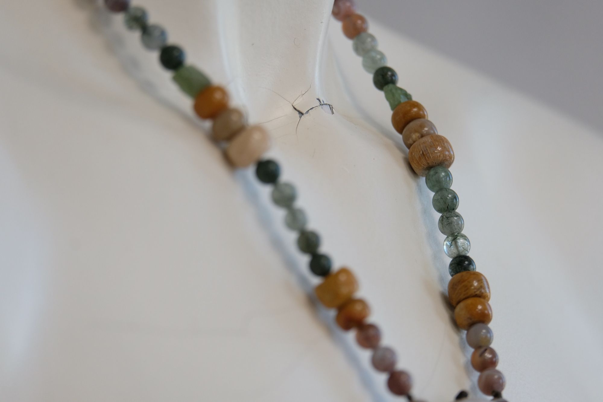 A necklace made of a silver moon, clear quartz crystal, earth-tone and green beads rests on a white mannequin