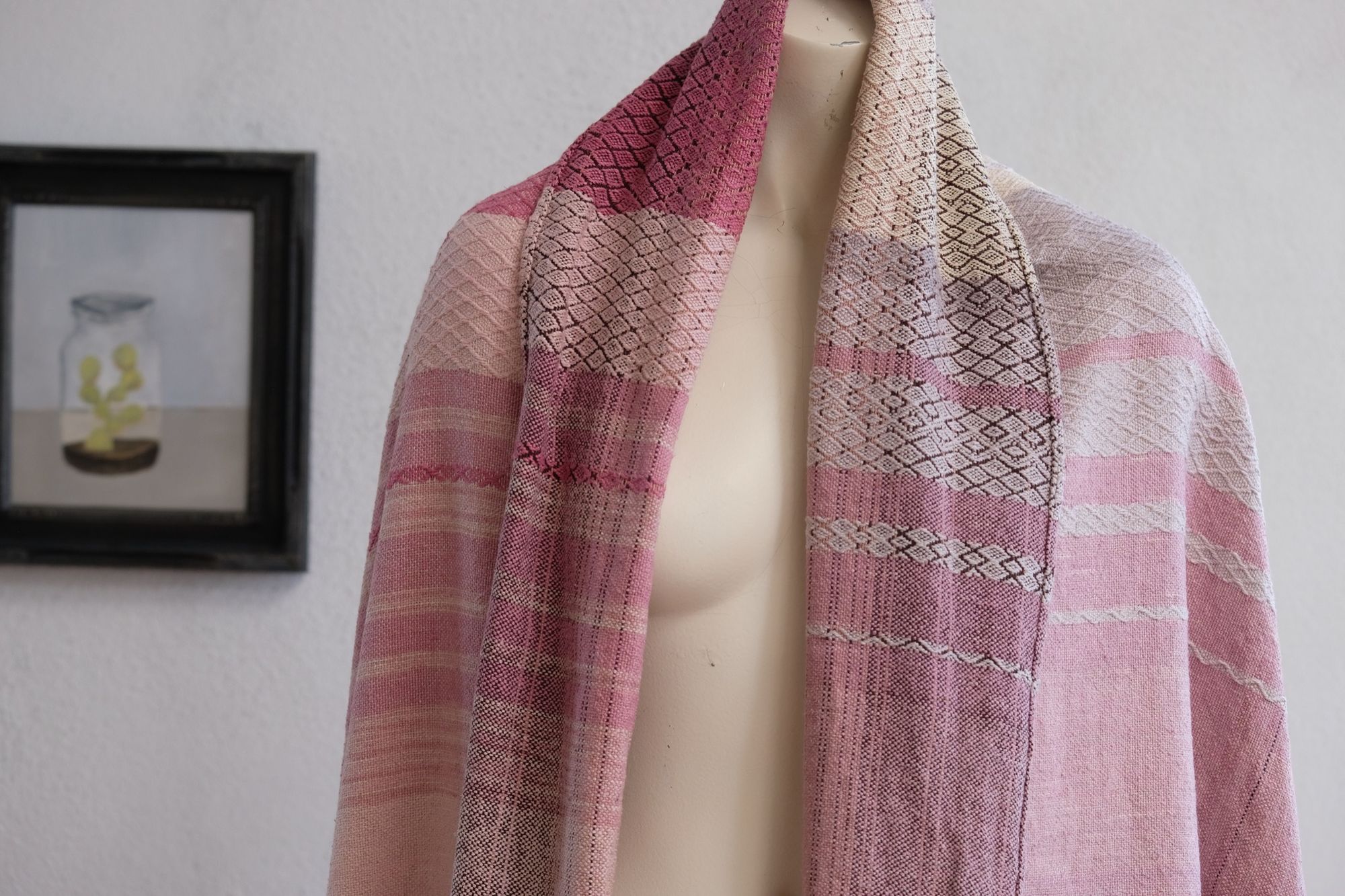 Handwoven fabric rests on a mannequin in a gallery. The fabric is naturally dyed with cochineal in all shades of pink and fuchsia