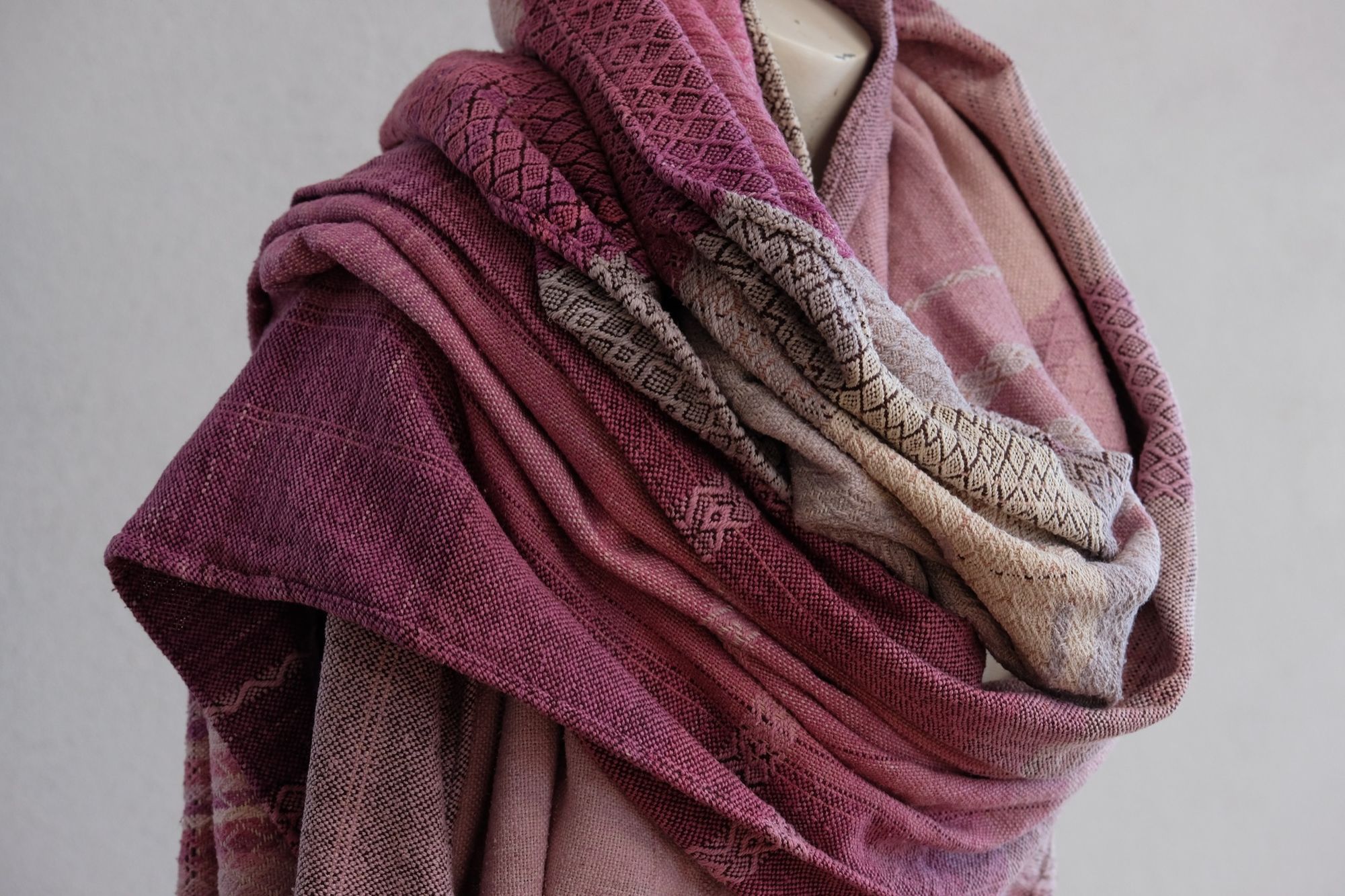 Handwoven fabric rests on a mannequin in a gallery. The fabric is naturally dyed with cochineal in all shades of pink and fuchsia