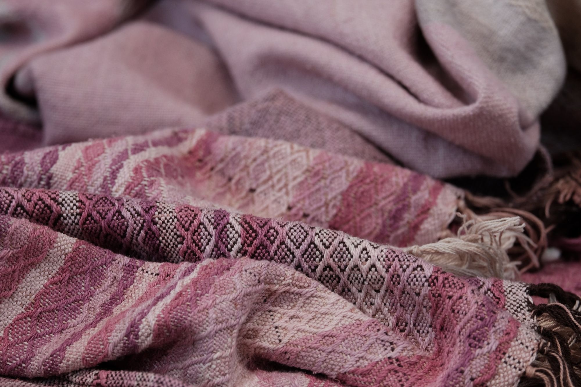 Handwoven fabric lays on a wood floor. The fabric is naturally dyed with cochineal in all shades of pink and fuchsia
