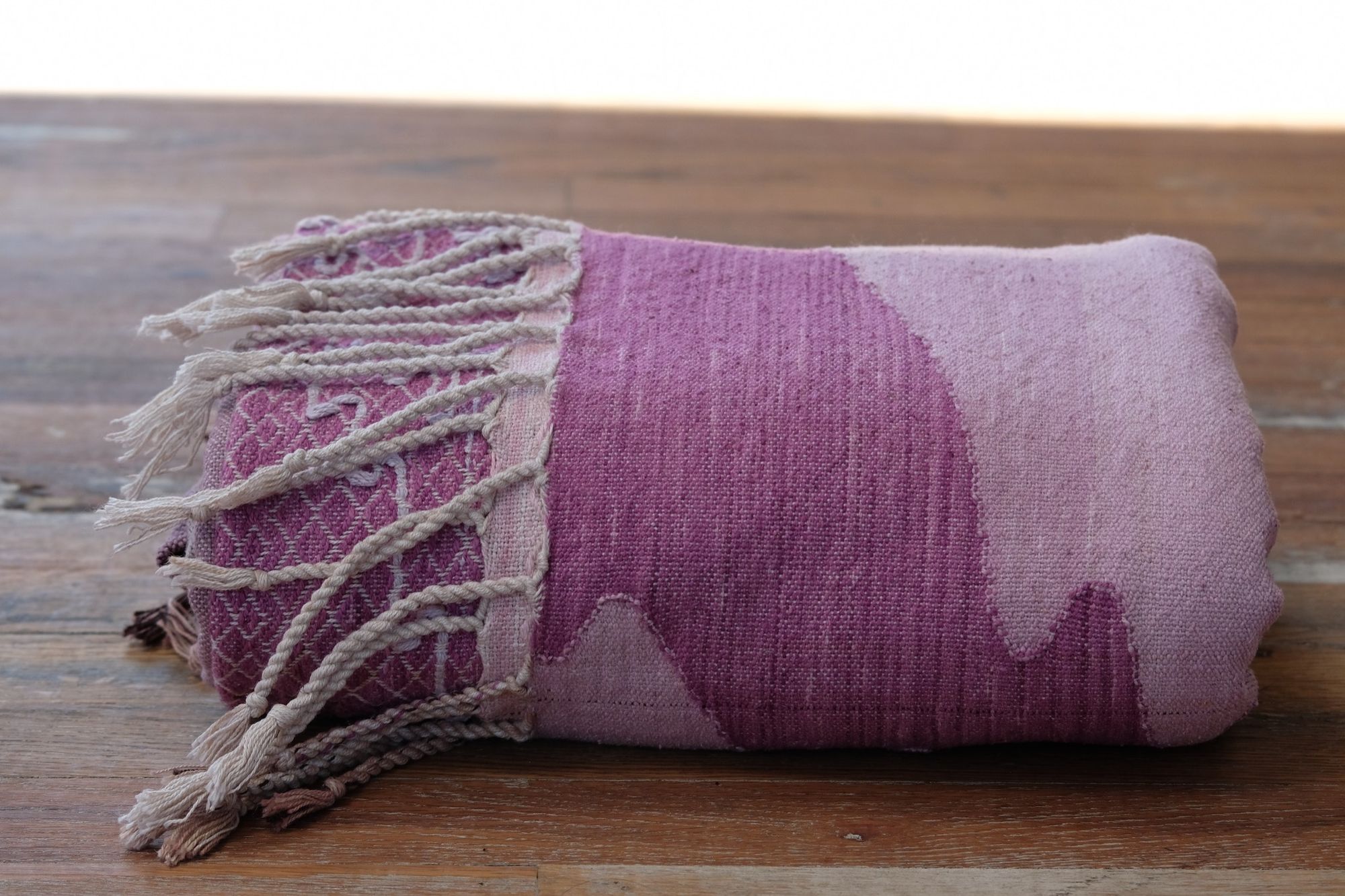 Handwoven fabric lays on a wooden floor in a gallery space. The fabric is naturally dyed with cochineal in all shades of pink and fuchsia with a design of a river and three moons on it