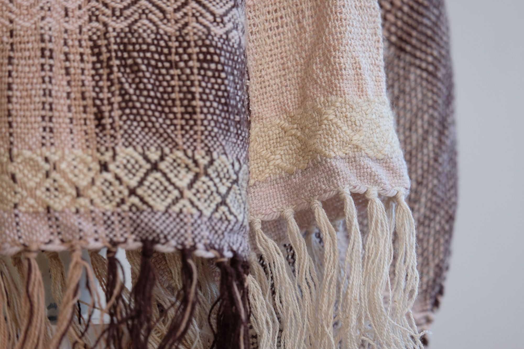 Handwoven scarf naturally dyed shades of pink, brown and green on a white mannequin in a white gallery space