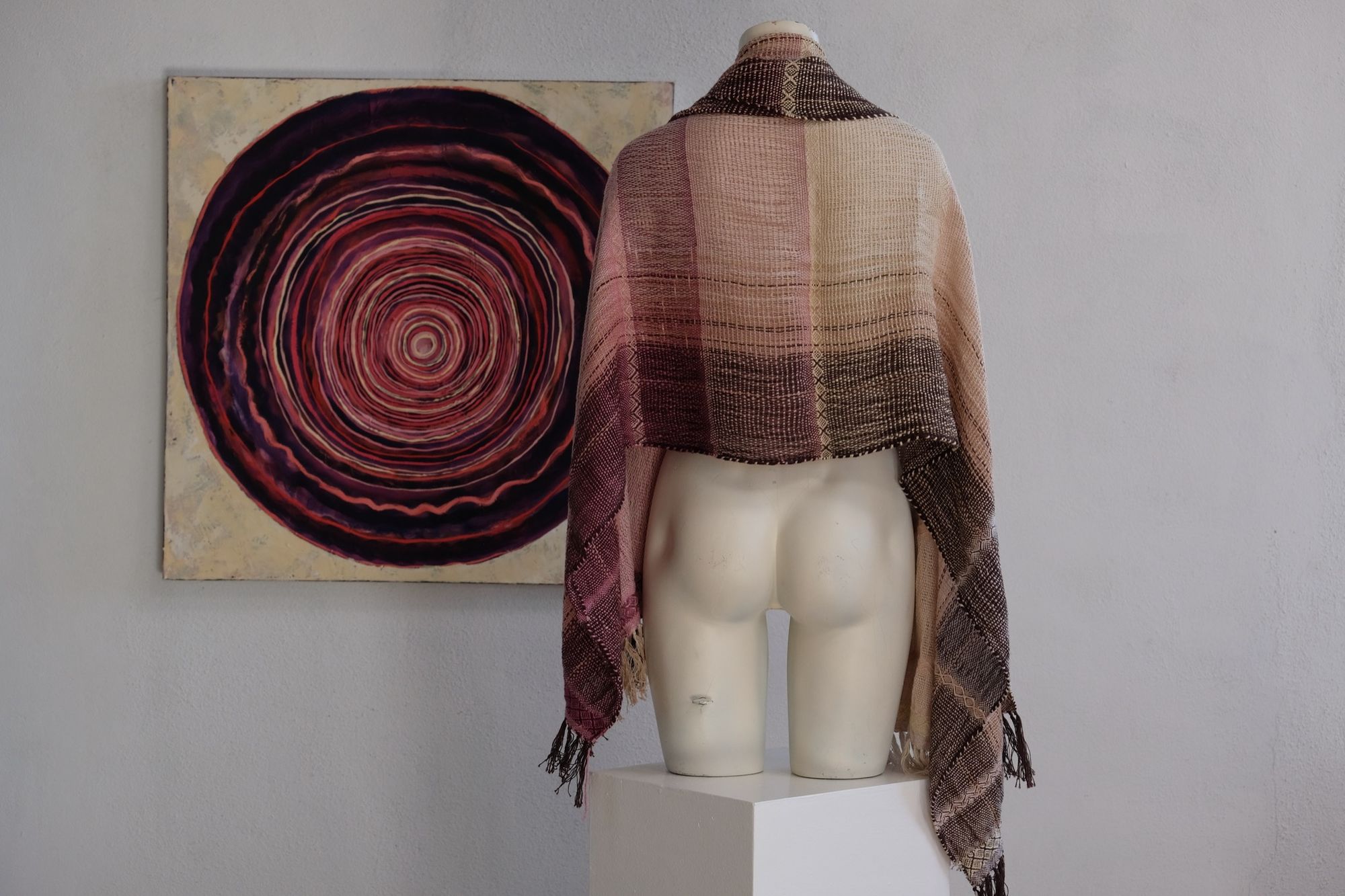 Handwoven scarf naturally dyed shades of pink, brown and green on a white mannequin in a white gallery space