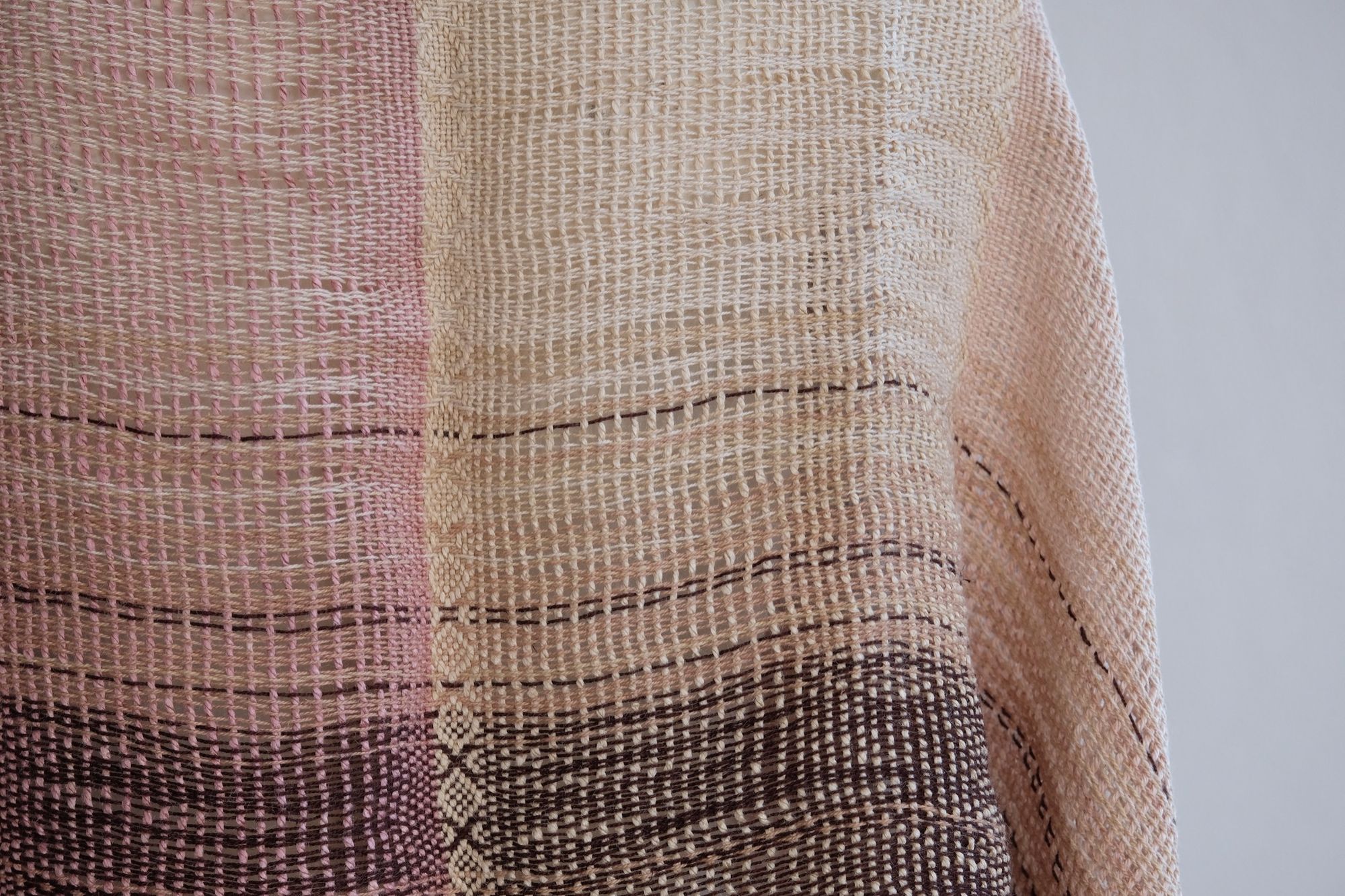 Handwoven scarf naturally dyed shades of pink, brown and green on a white mannequin in a white gallery space