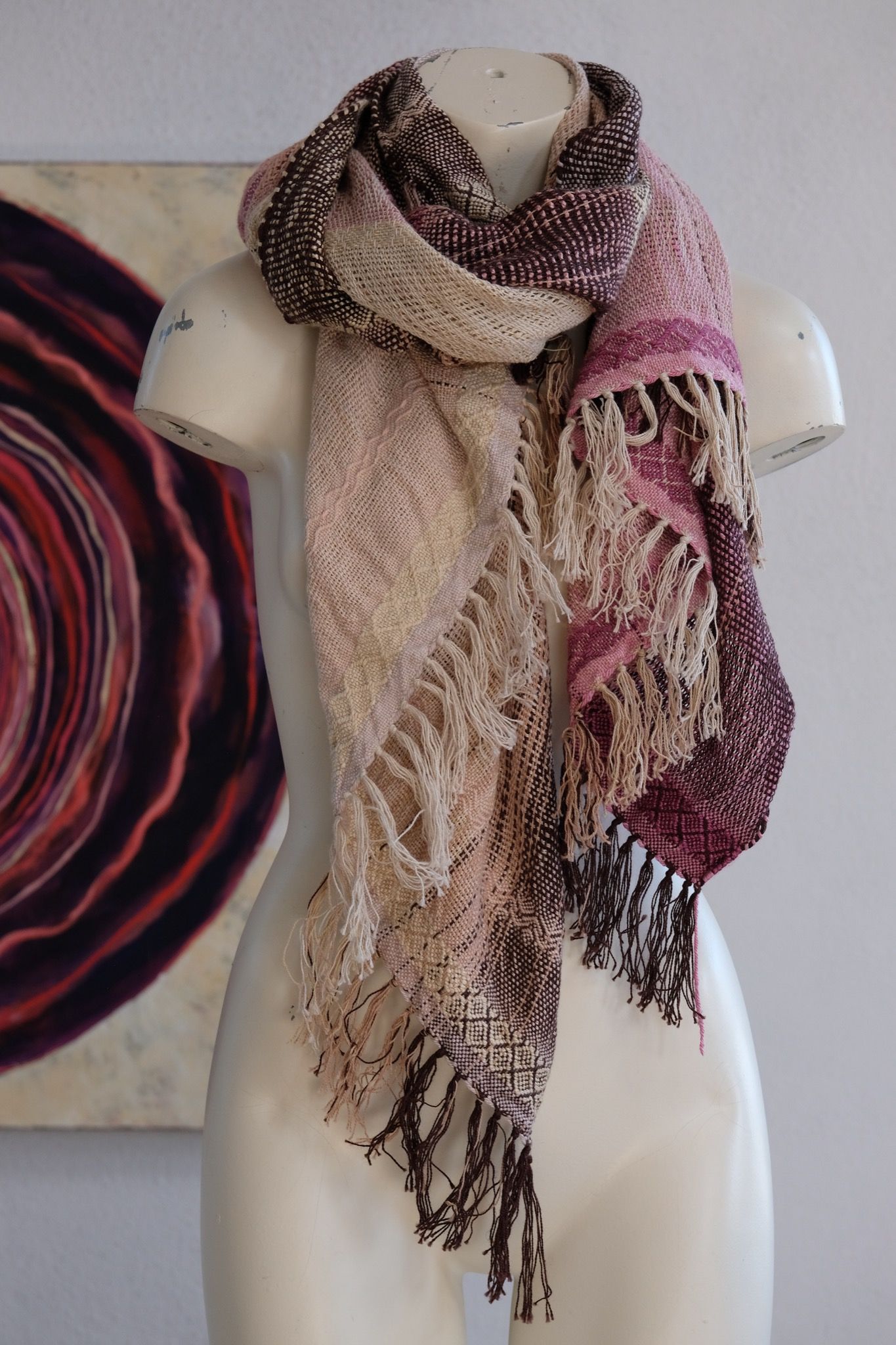 Handwoven scarf naturally dyed shades of pink, brown and green on a white mannequin in a white gallery space