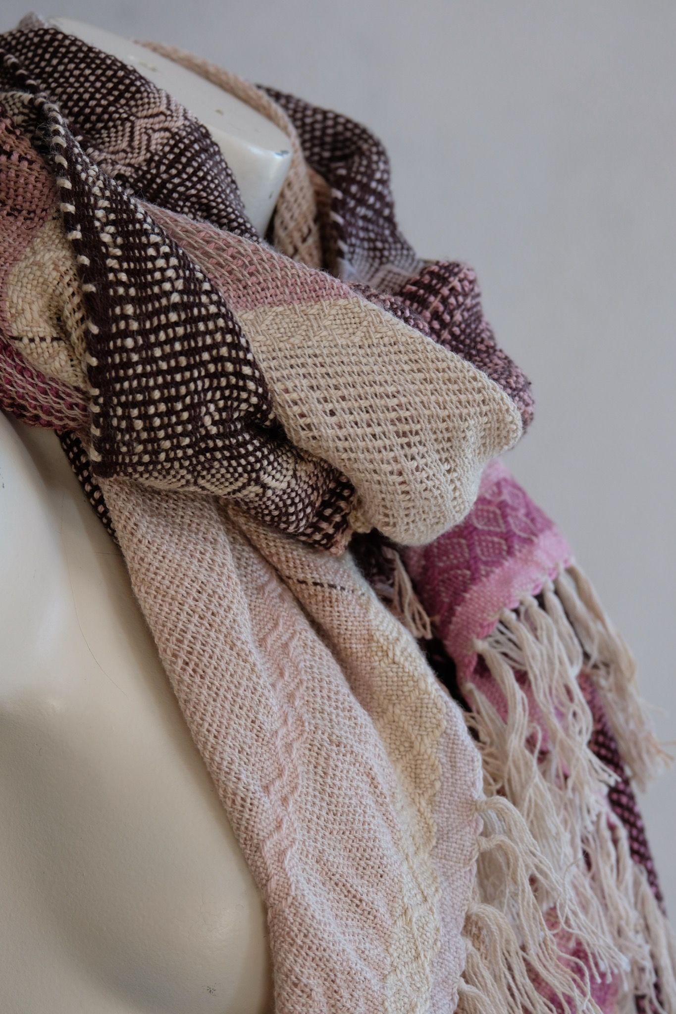 Handwoven scarf naturally dyed shades of pink, brown and green on a white mannequin in a white gallery space