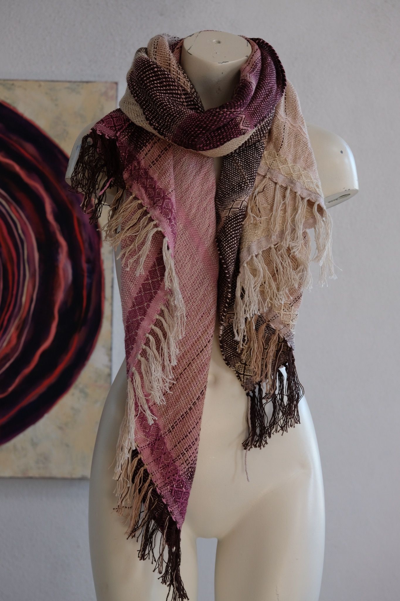 Handwoven scarf naturally dyed shades of pink, brown and green on a white mannequin in a white gallery space