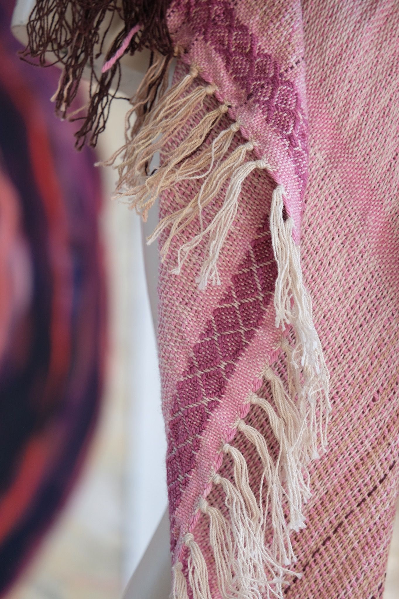 Handwoven scarf naturally dyed shades of pink, brown and green on a white mannequin in a white gallery space