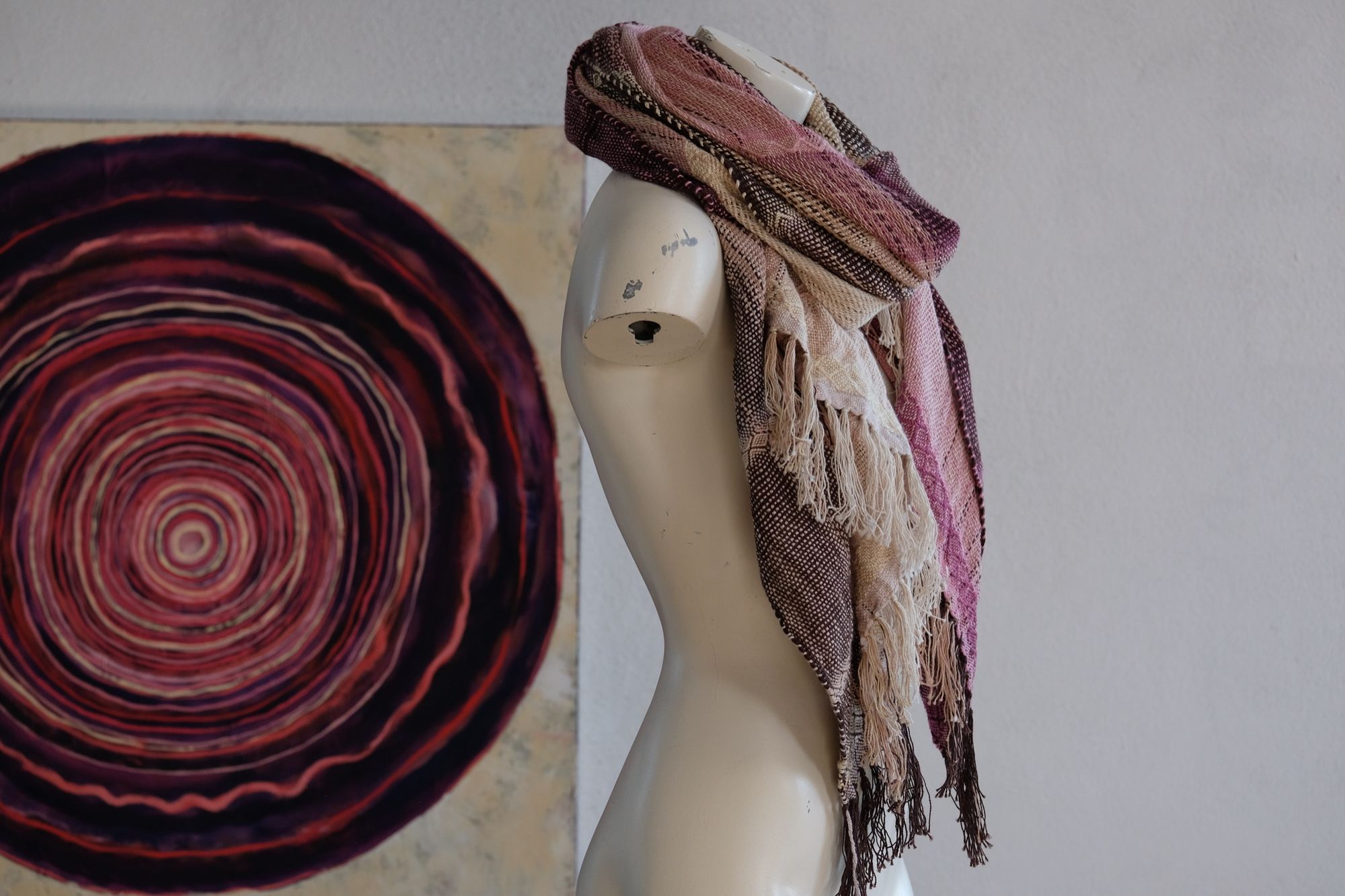 Handwoven scarf naturally dyed shades of pink, brown and green on a white mannequin in a white gallery space