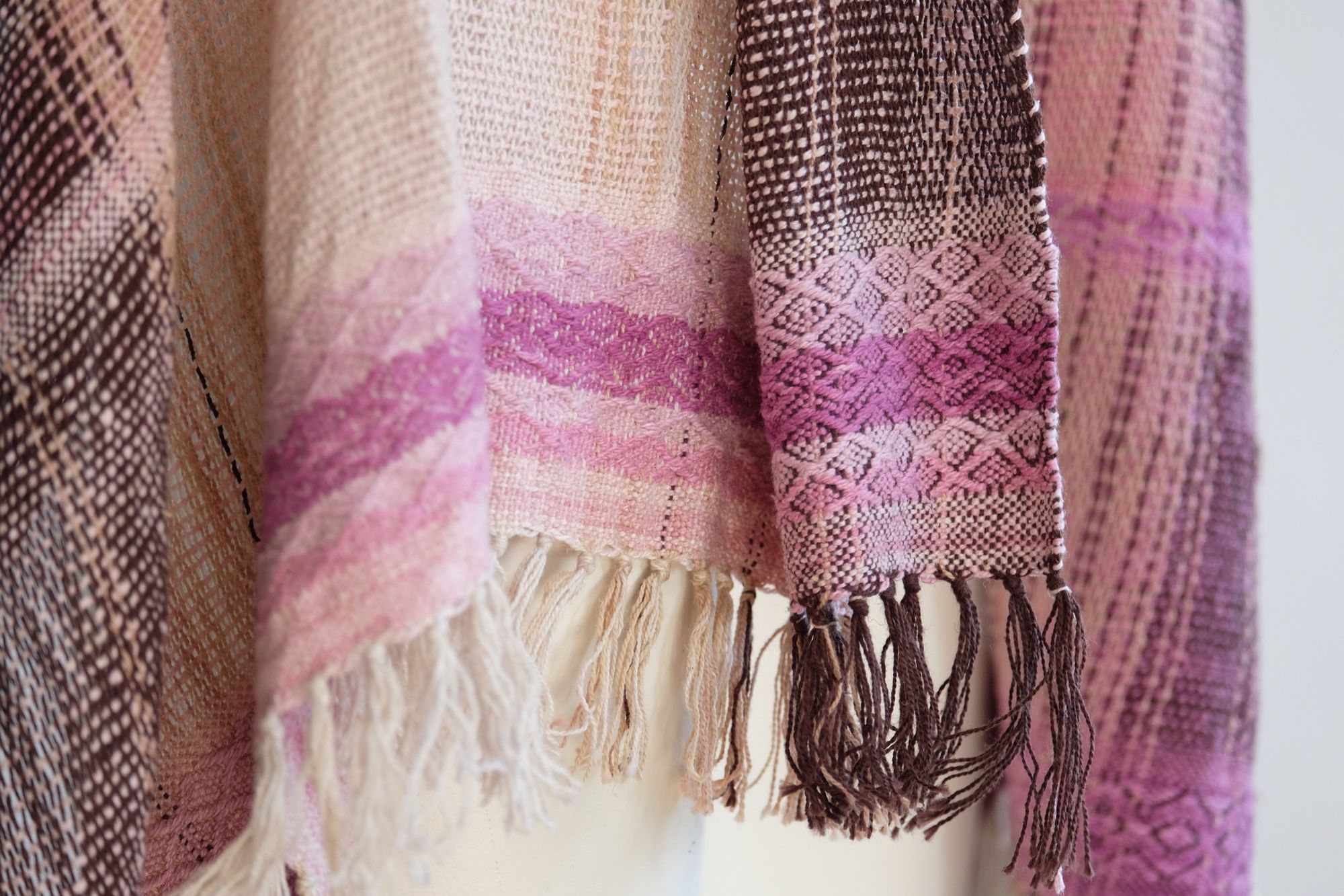 Handwoven scarf naturally dyed shades of pink and fuchsia on a white mannequin in a white gallery space