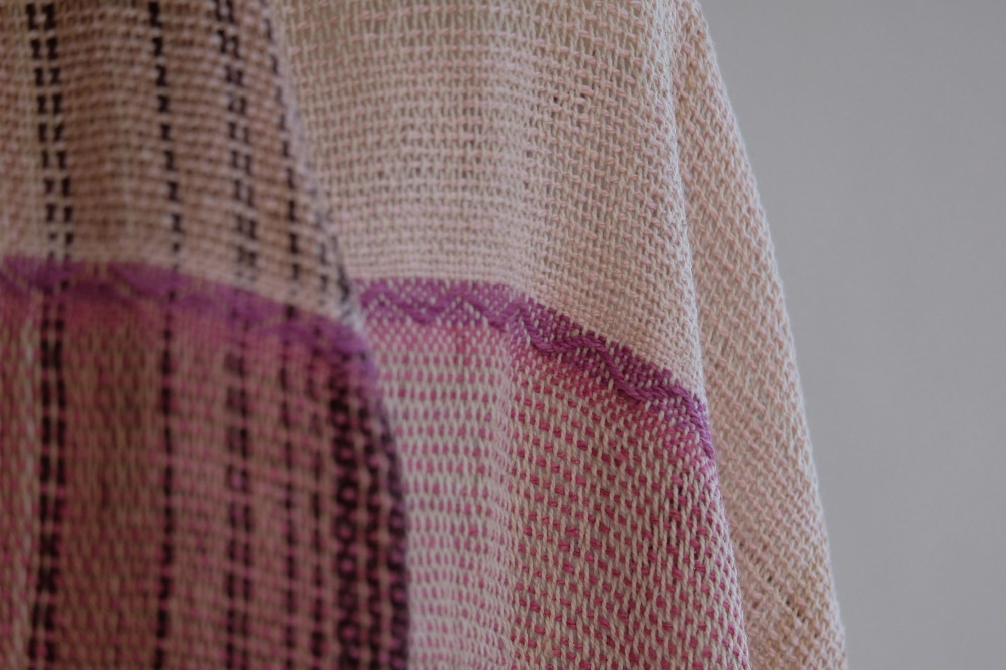 Handwoven scarf naturally dyed shades of pink and fuchsia on a white mannequin in a white gallery space