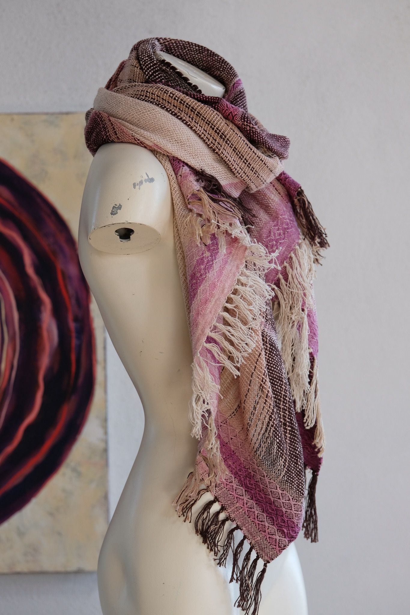 Handwoven scarf naturally dyed shades of pink and fuchsia on a white mannequin in a white gallery space