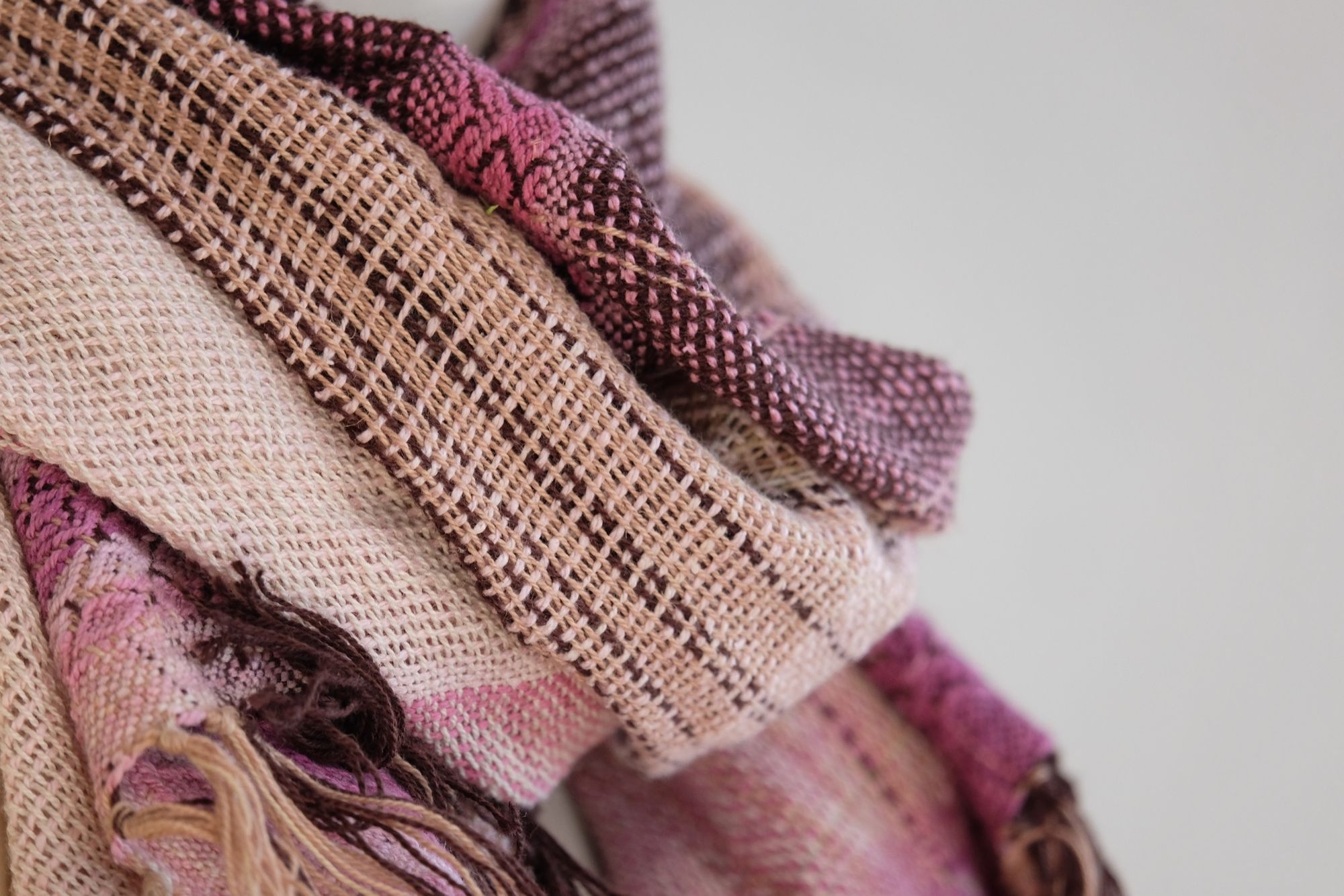 Handwoven scarf naturally dyed shades of pink and fuchsia on a white mannequin in a white gallery space