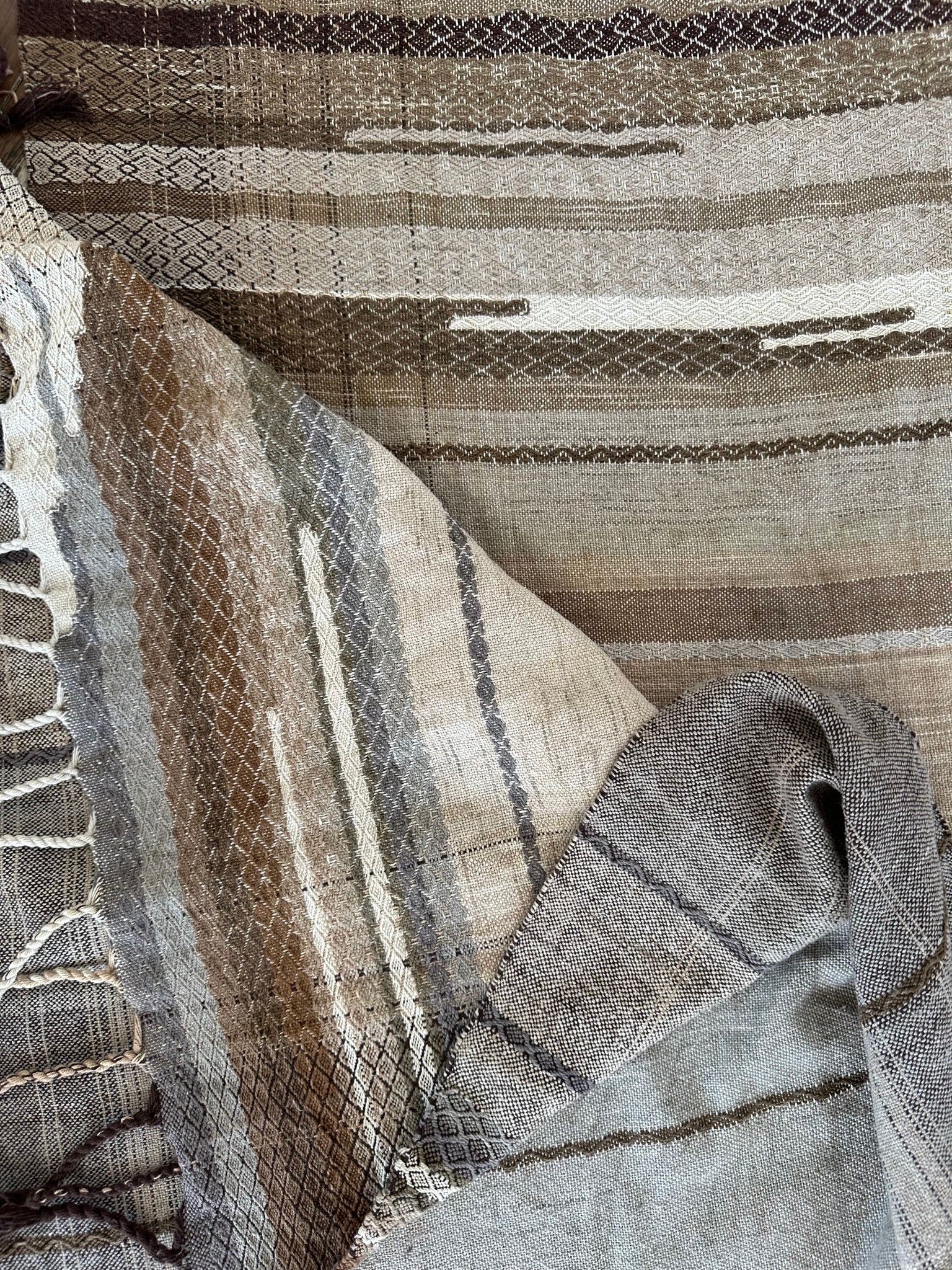 Details of a handwoven naturally dyed raw silken organic cotton linen shawl with diamond pattern and stripes of gradations of grey, brown, tan and white.