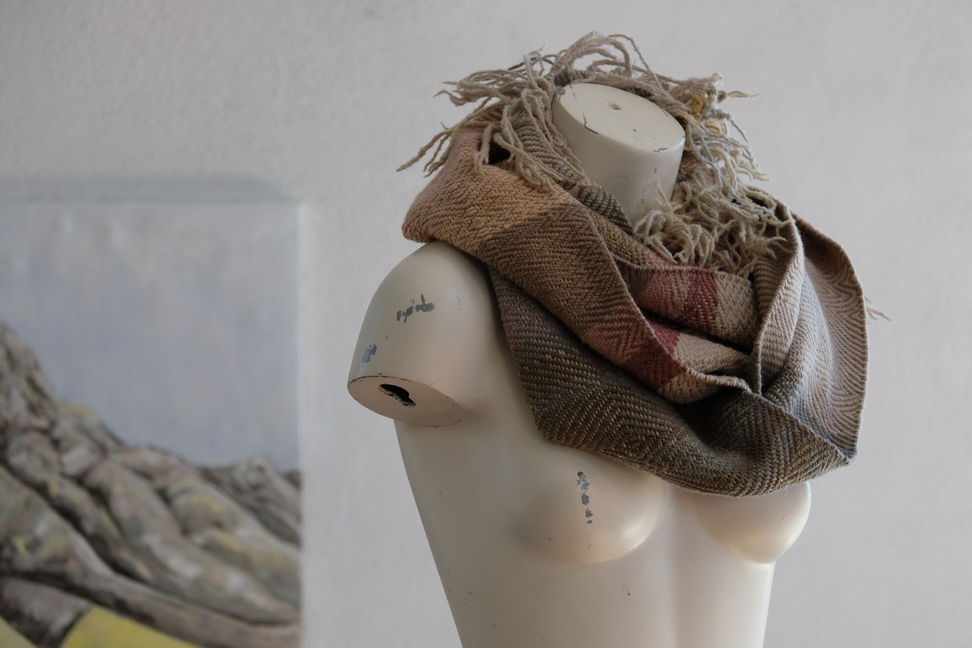 A white painted mannequin torso wears a handwoven naturally dyed highly textured and fringed loop scarf in soft shades of pink, grey, yellow and tan
