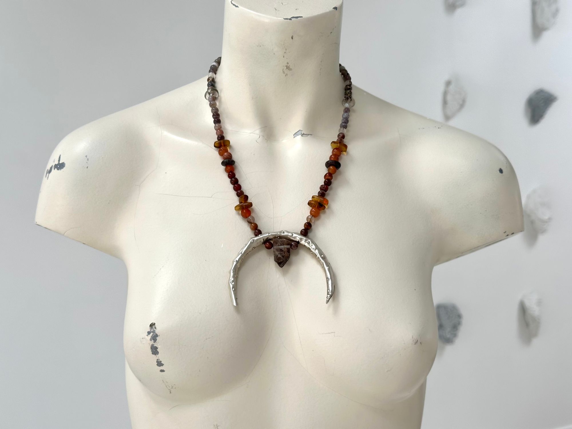 A painted white mannequin wears a necklace with a silver Crescent moon shape And beads of Amber Quartz and agate in soft warm earth tones