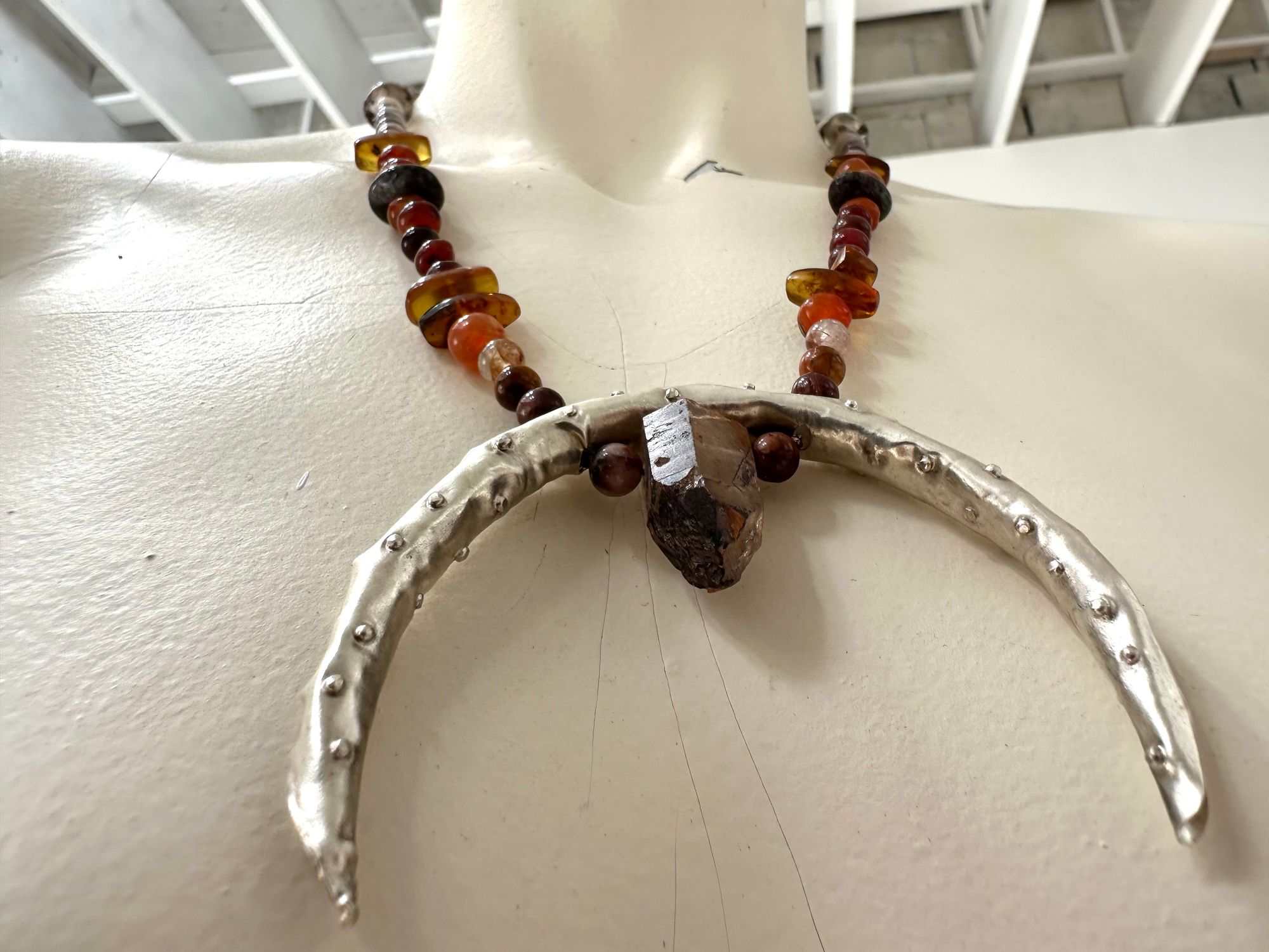 A painted white mannequin wears a necklace with a silver Crescent moon shape And beats of Amber Quartz and agate in soft warm earth tones