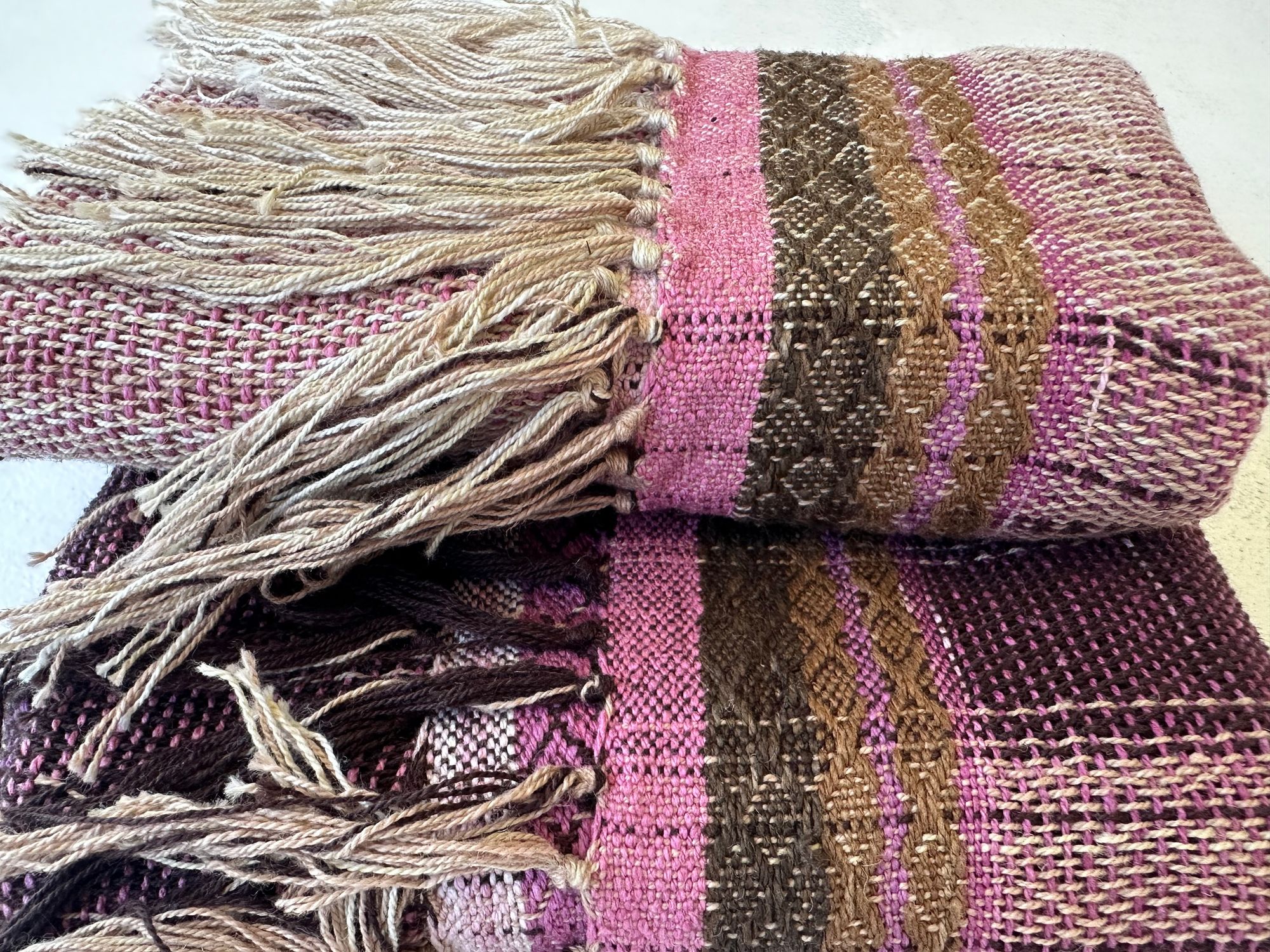 A folded piece of cloth rests on a white floor. The cloth is handwoven out of organic cotton linen and cochineal dyed raw Silk