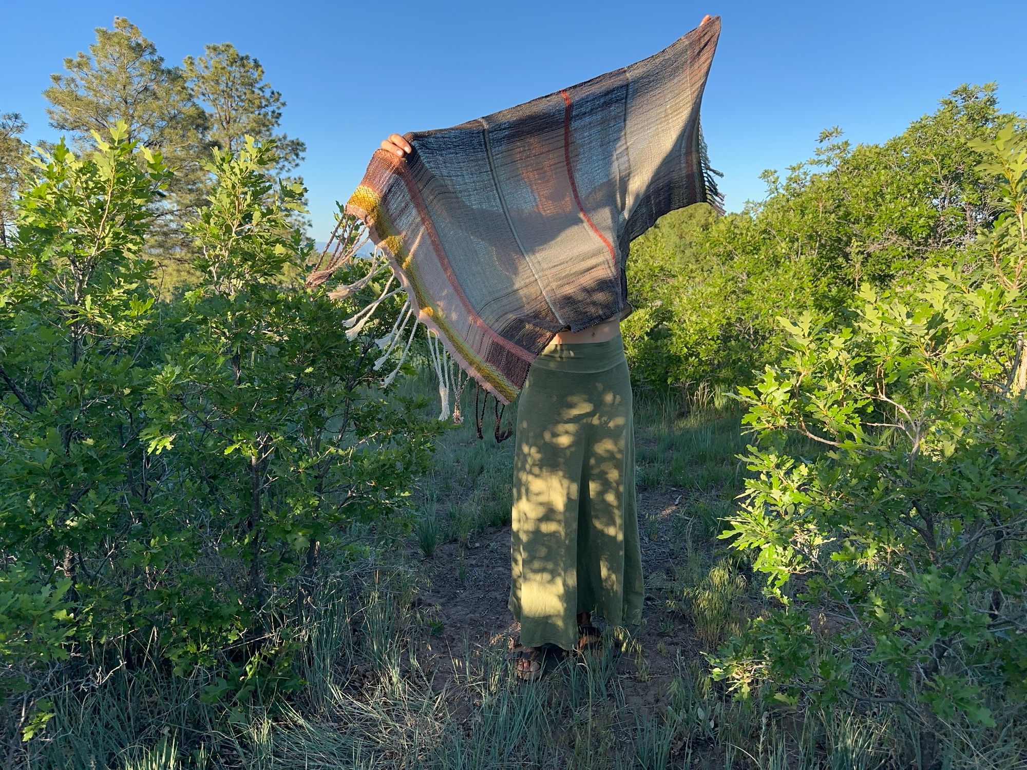 A woman standing in a scrub Oak Grove is wearing a lightly woven, naturally dyed raw silk and organic cotton linen Shawl in pink, yellow and brown 