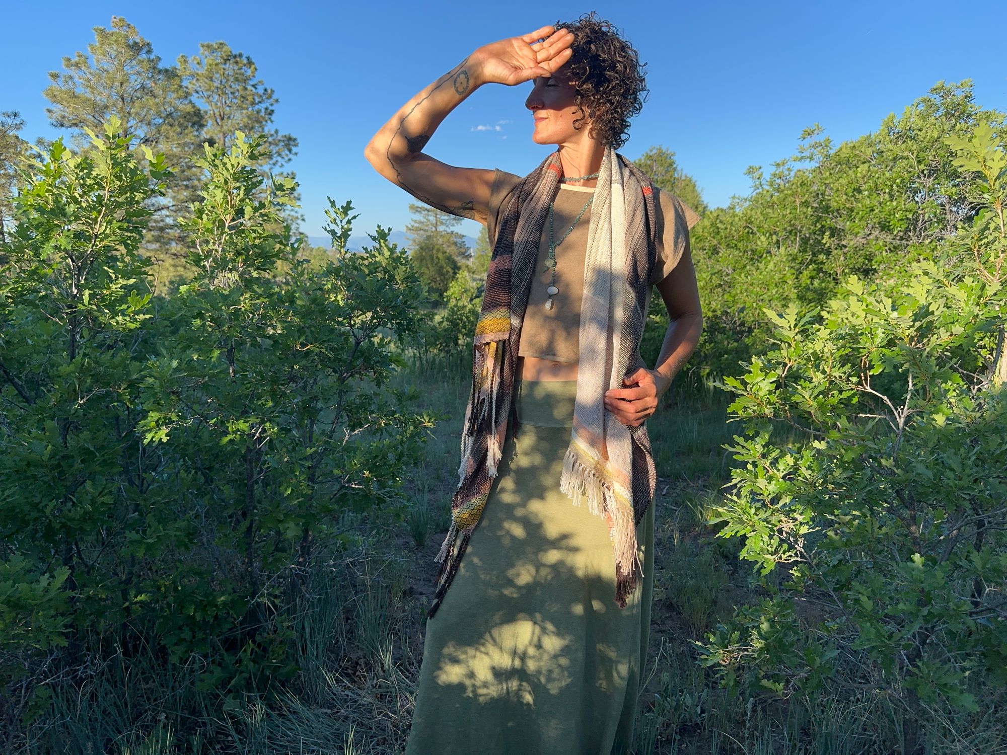 A woman standing in a scrub Oak Grove is wearing a lightly woven, naturally dyed raw silk and organic cotton linen Shawl in pink, yellow and brown 