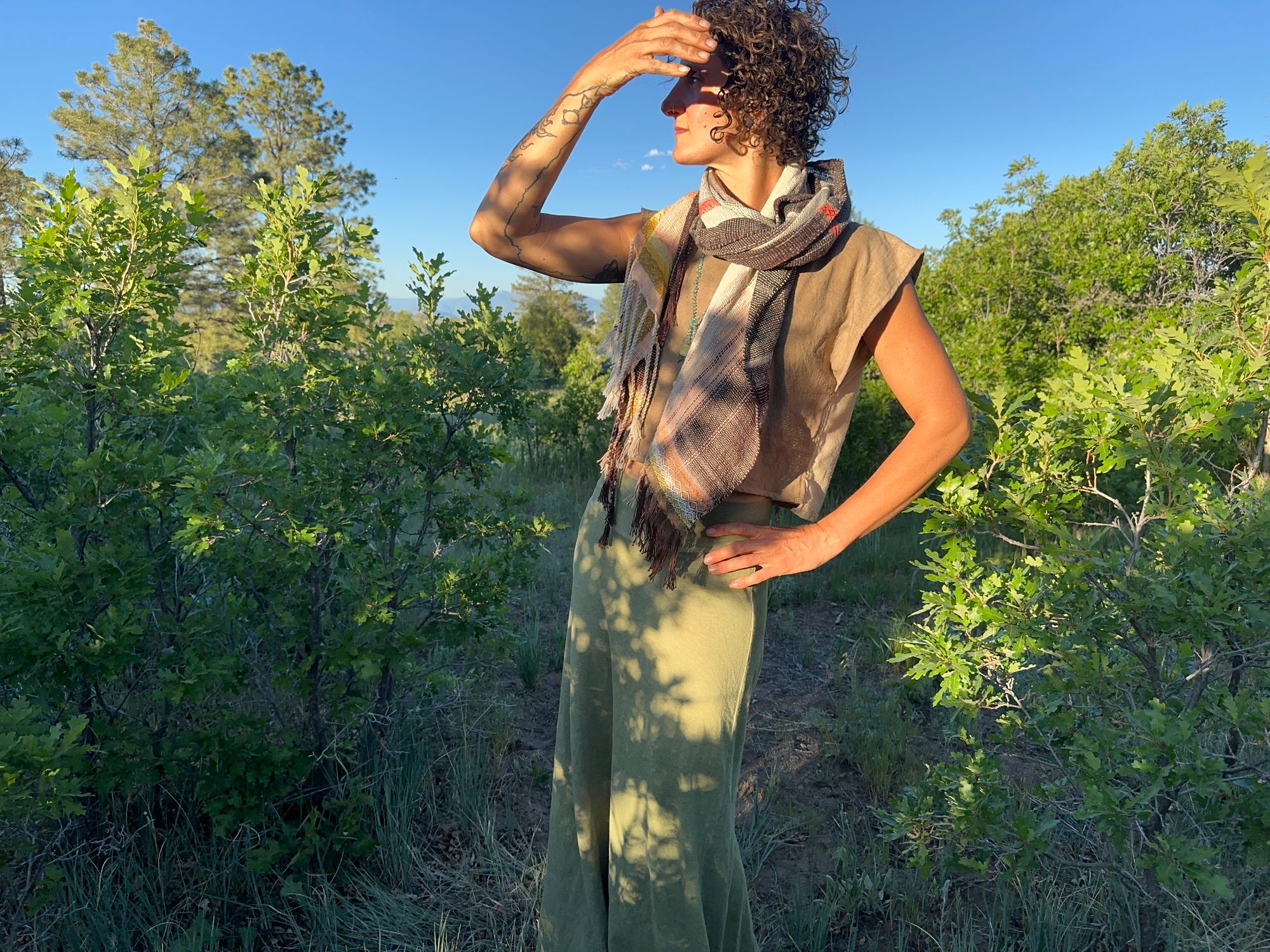 A woman standing in a scrub Oak Grove is wearing a lightly woven, naturally dyed raw silk and organic cotton linen Shawl in pink, yellow and brown 