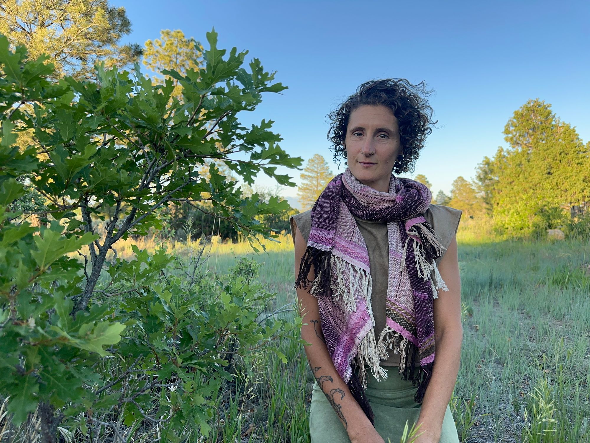 A woman in a brown shirt and green skirt wears a handwoven Naturally dyed pink shawl in the forest