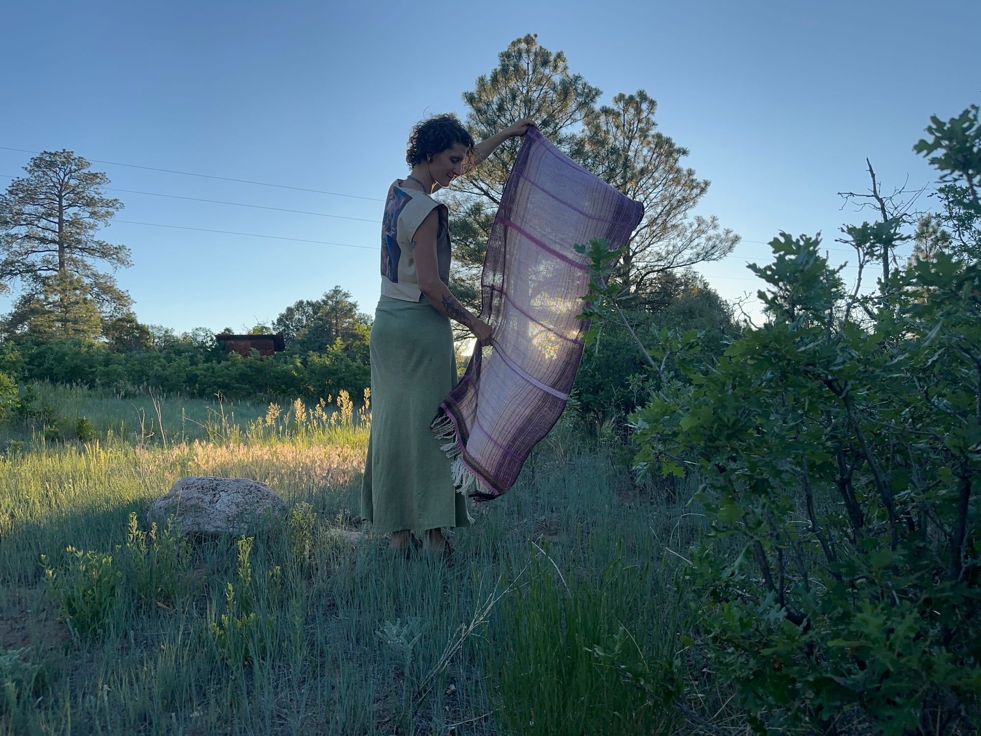 A woman in a brown shirt and green skirt wears a handwoven Naturally dyed pink shawl in the forest