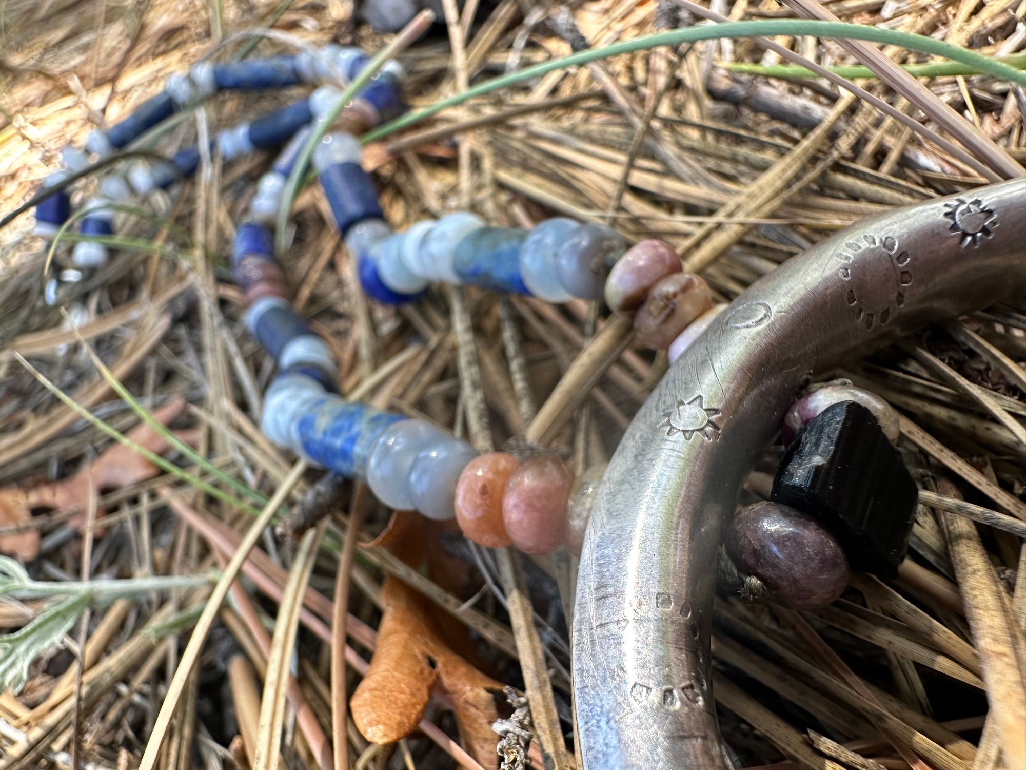 A necklace made of semi precious stones and a solid silver moon lays on a lichen covered rock