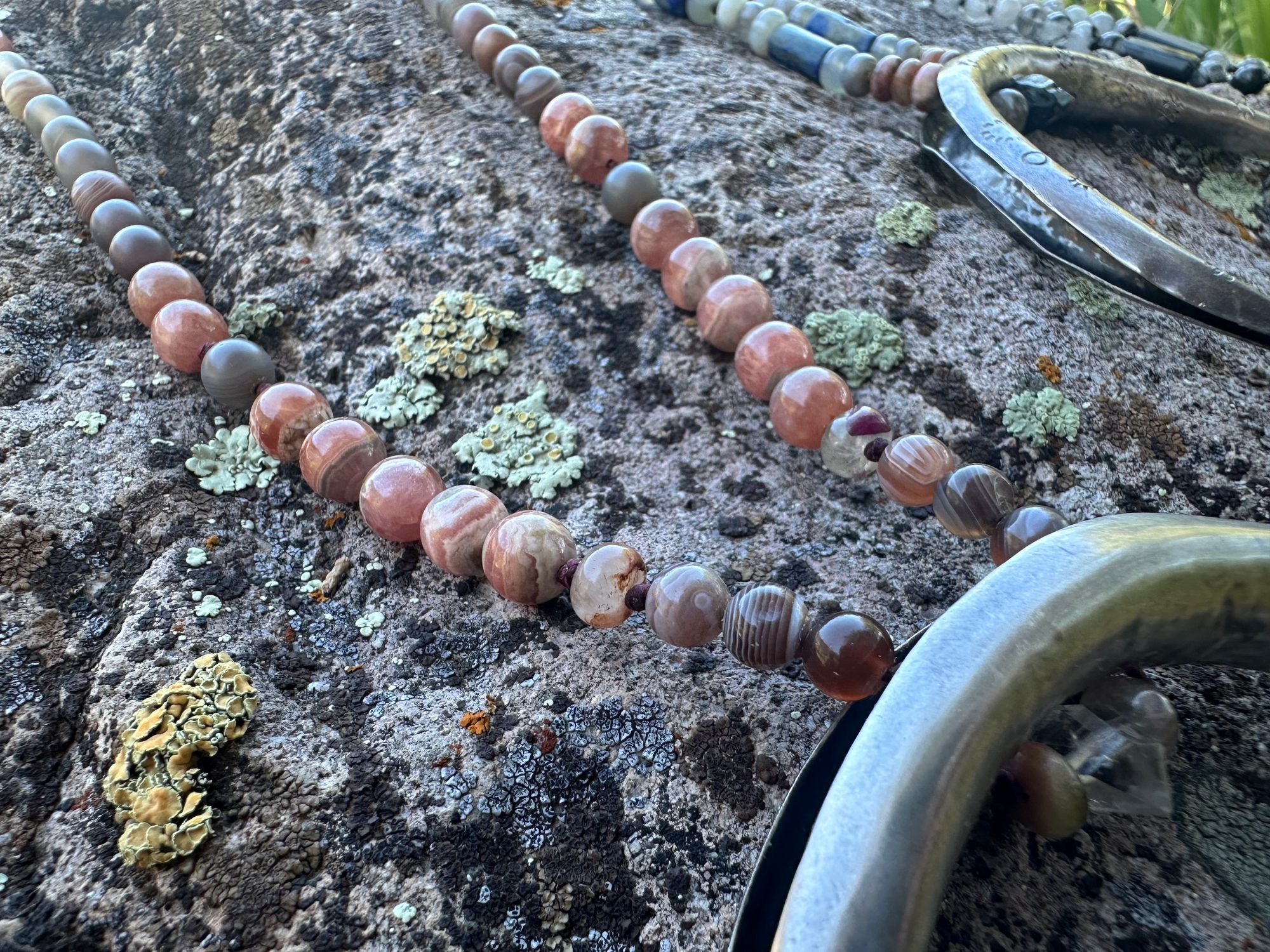 A necklace made of semi precious stones and a solid silver moon lays on a lichen covered rock