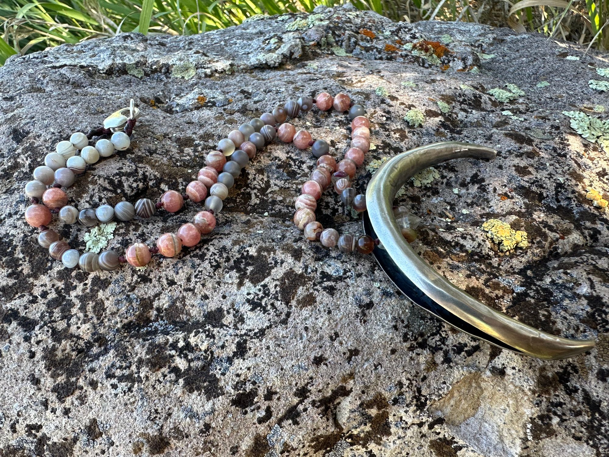 A necklace made of semi precious stones and a solid silver moon lays on a lichen covered rock