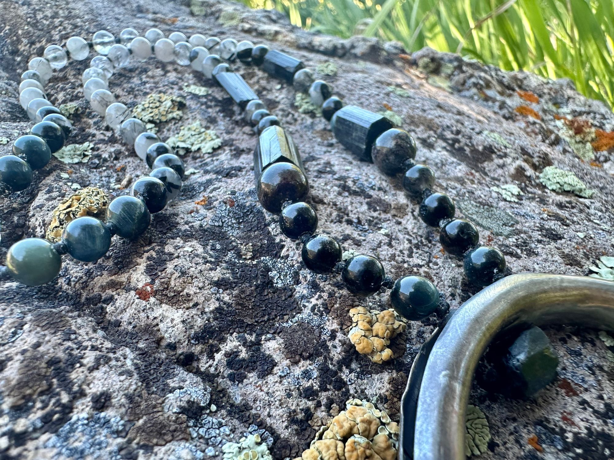 A necklace made of semi precious stones and a solid silver moon lays on a lichen covered rock