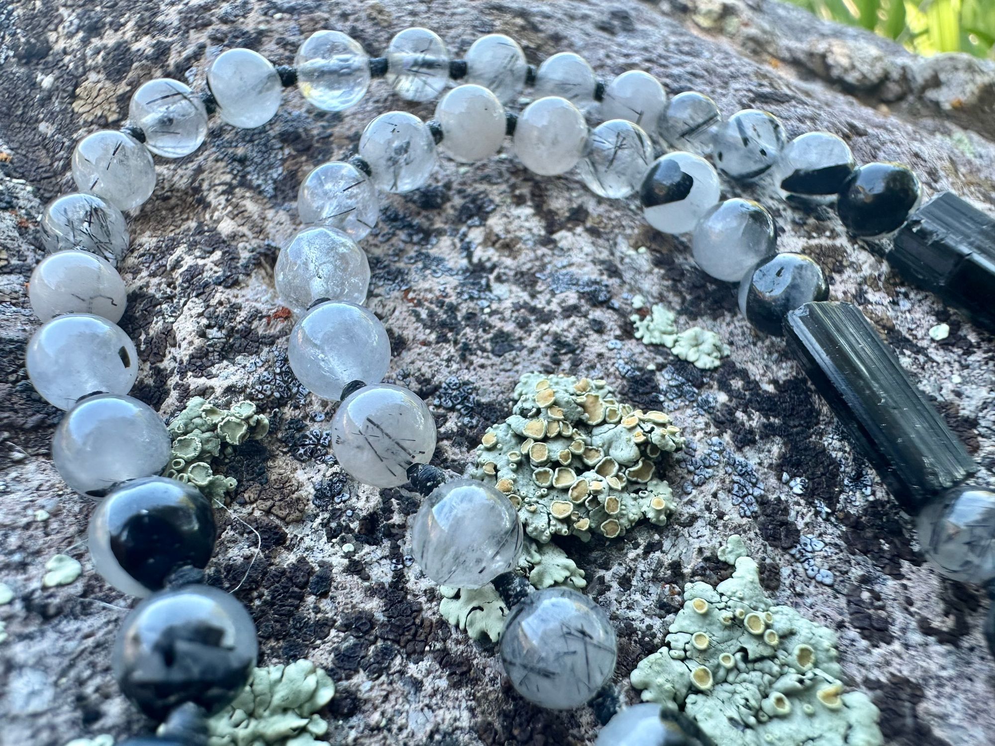 A necklace made of semi precious stones and a solid silver moon lays on a lichen covered rock