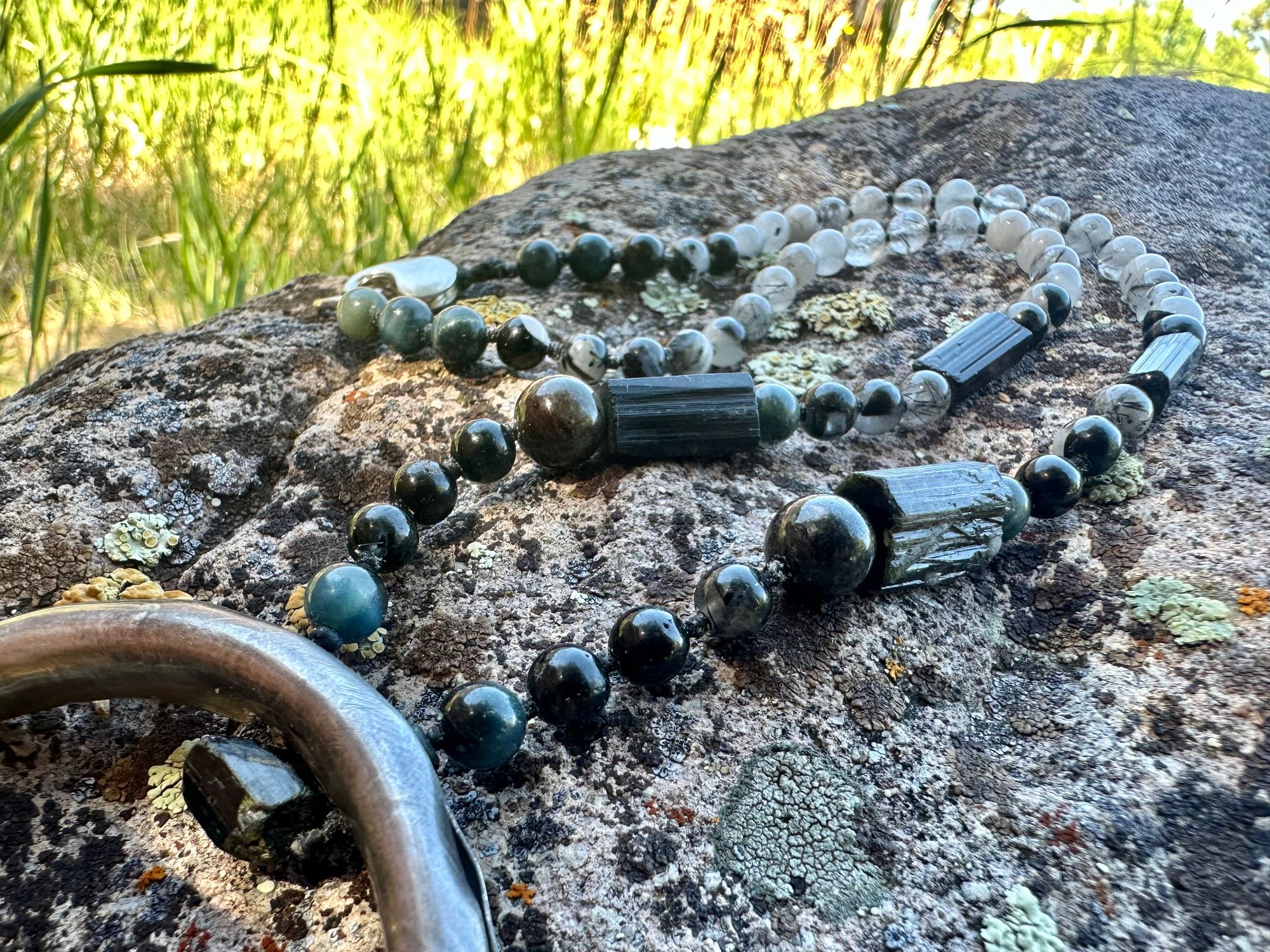 A necklace made of semi precious stones and a solid silver moon lays on a lichen covered rock