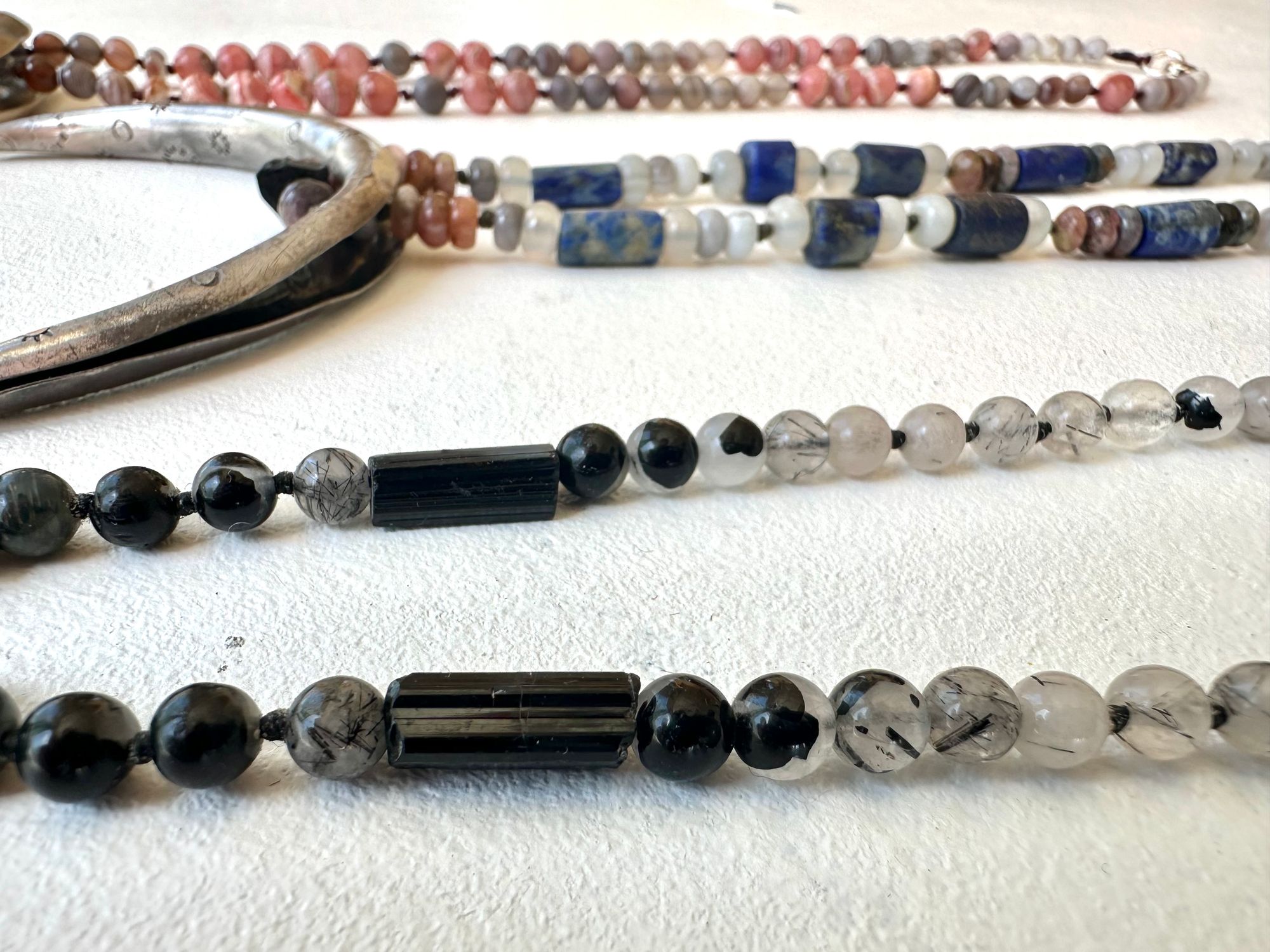 A necklace made of a solid silver moon and semi precious stone beads rests on a white floor