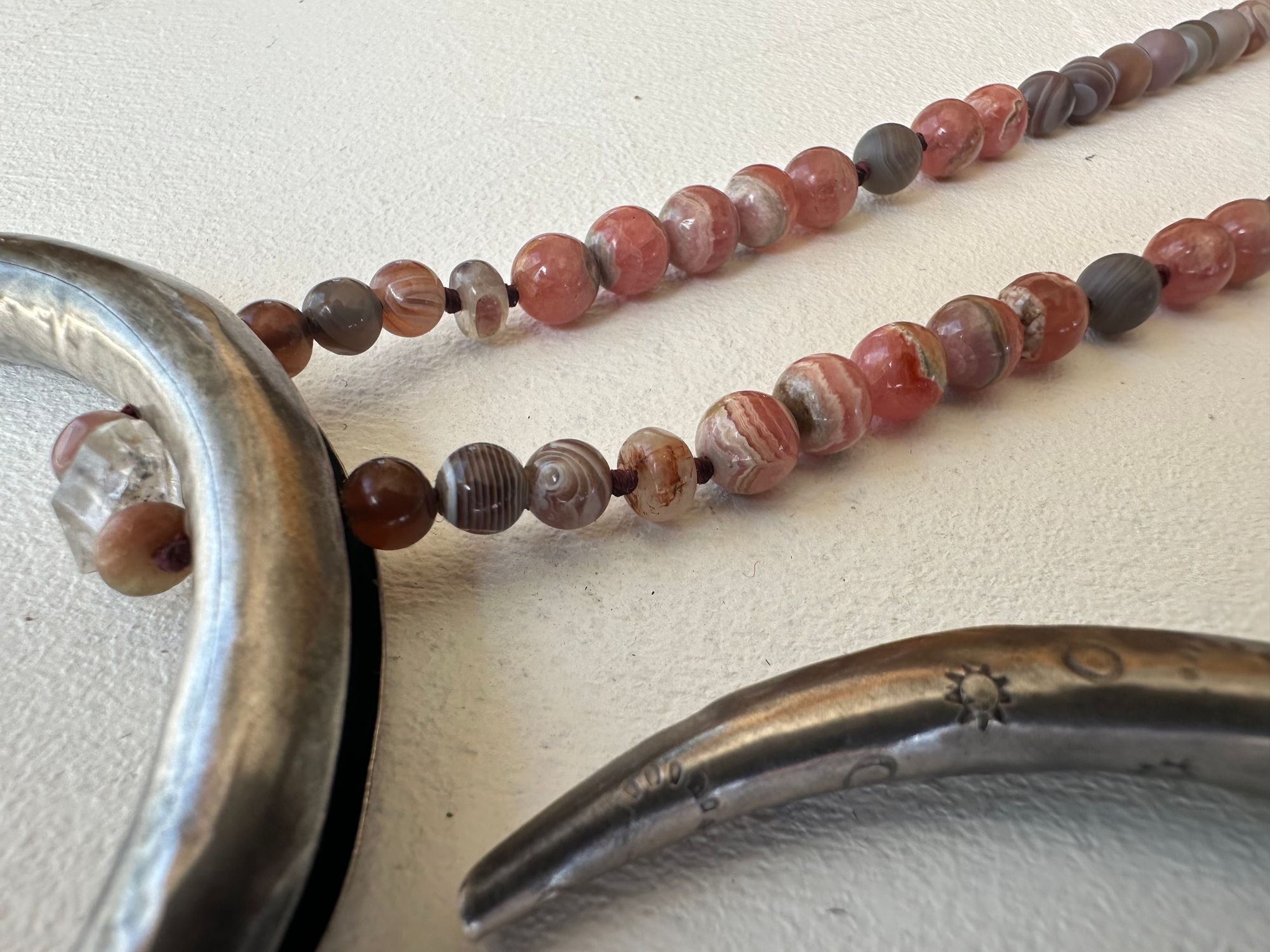 A necklace made of a solid silver moon and semi precious stone beads rests on a white floor