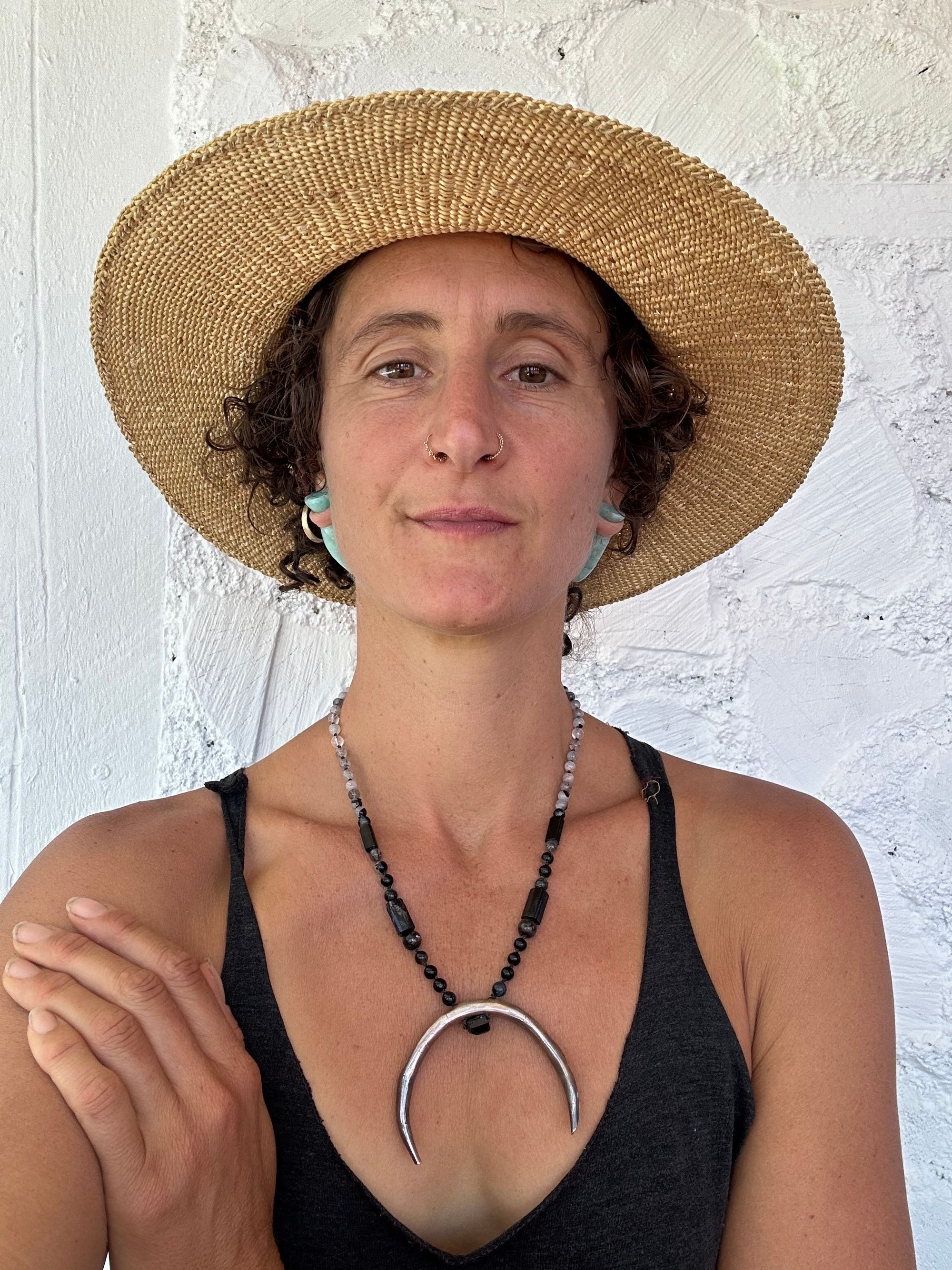 A woman wears a necklace with a sterling silver moon and semi precious stone beads, against a white painted cordwood Wall