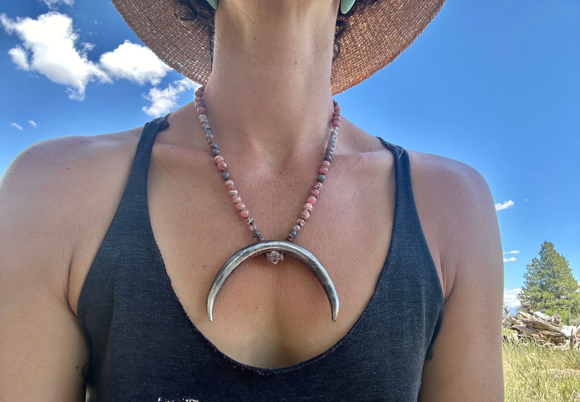 A woman wears a necklace with a sterling silver moon and semi precious stone beads, in the forest