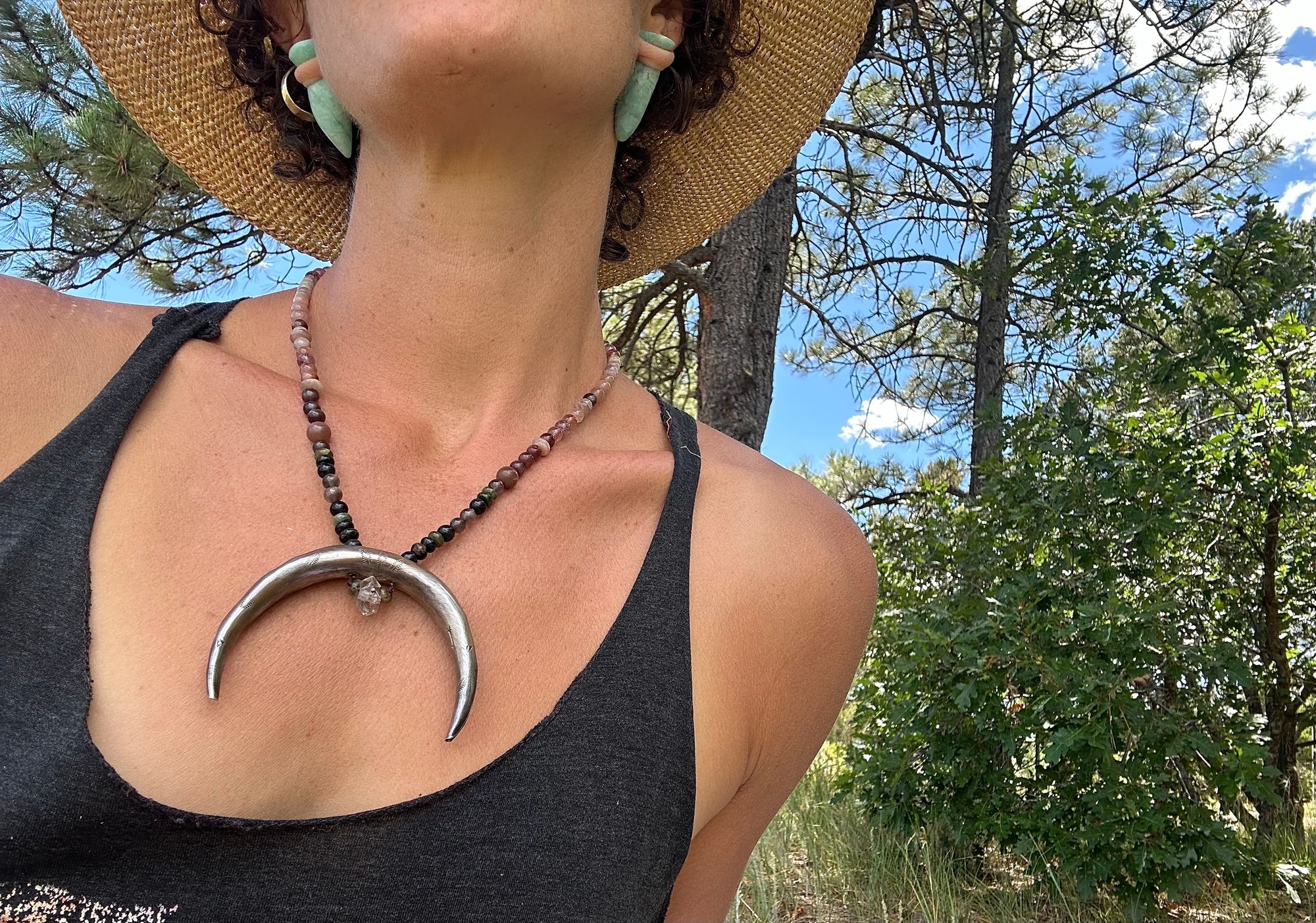 A woman wears a necklace with a sterling silver moon and semi precious stone beads, in the forest