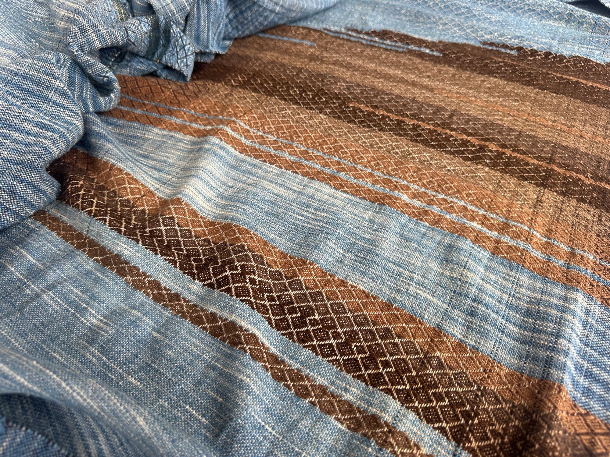 a 4.6 meter piece of handwoven fabric that is indigo blue and deep walnut dyed brown lays on a white floor