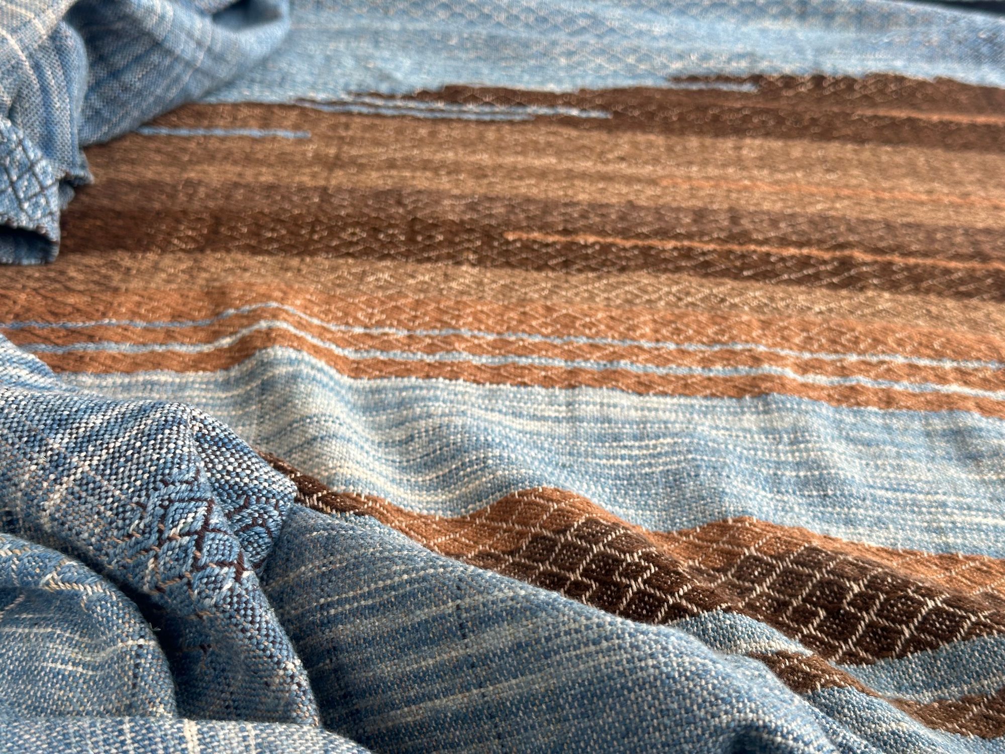 a 4.6 meter piece of handwoven fabric that is indigo blue and deep walnut dyed brown lays on a white floor