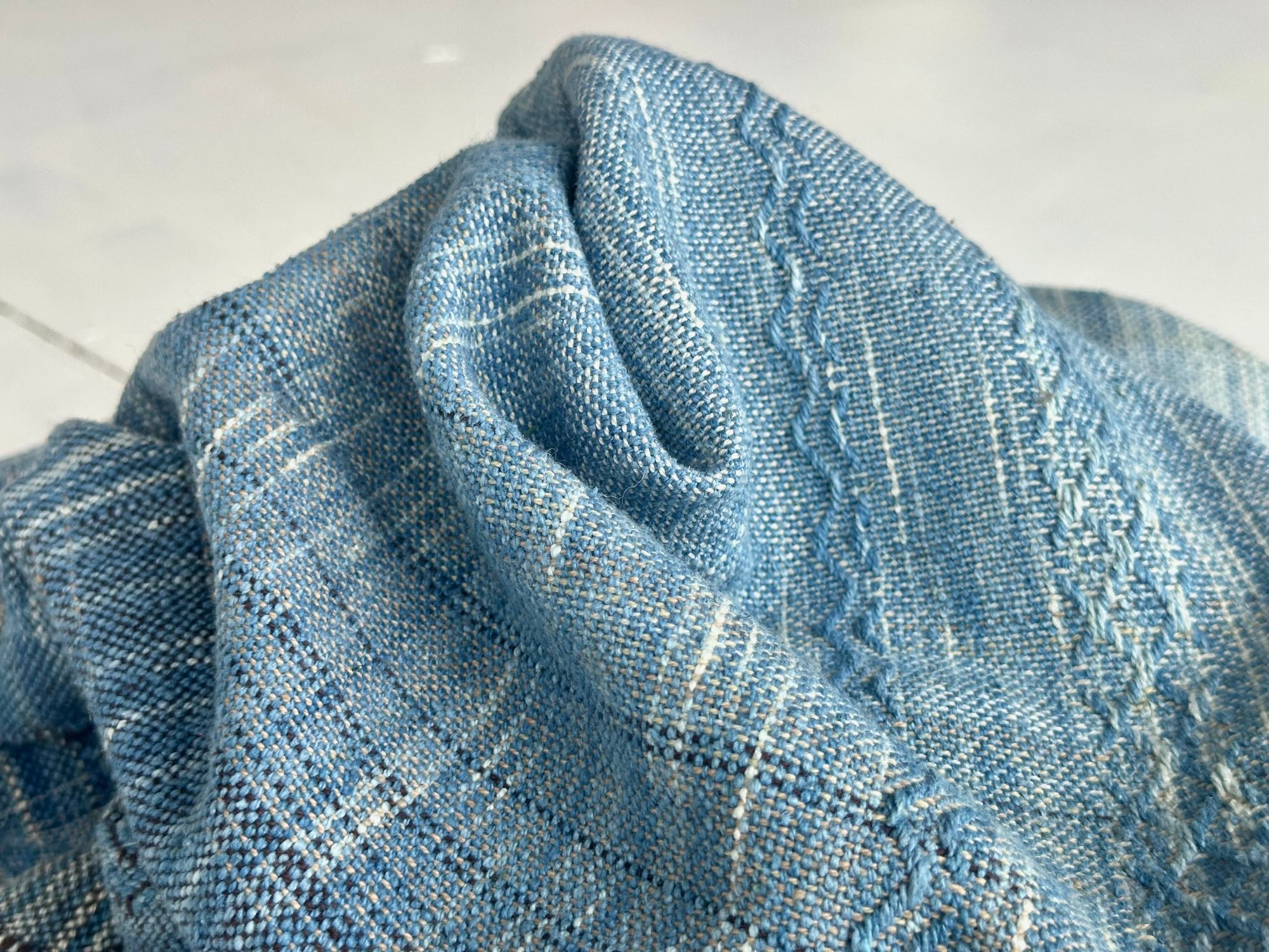 a 4.6 meter piece of handwoven fabric that is indigo blue and deep walnut dyed brown lays on a white floor