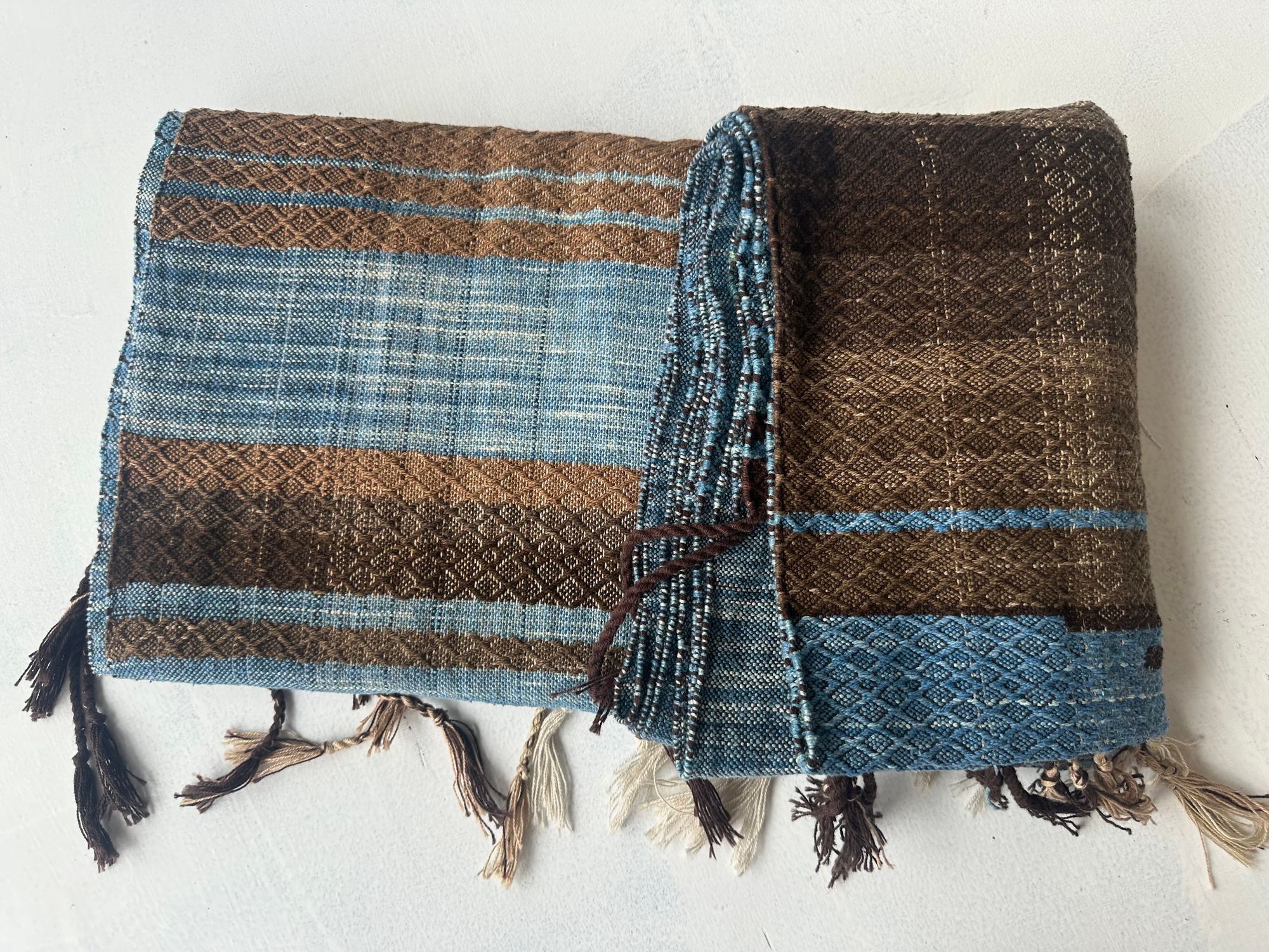 a 4.6 meter piece of handwoven fabric that is indigo blue and deep walnut dyed brown lays on a white floor