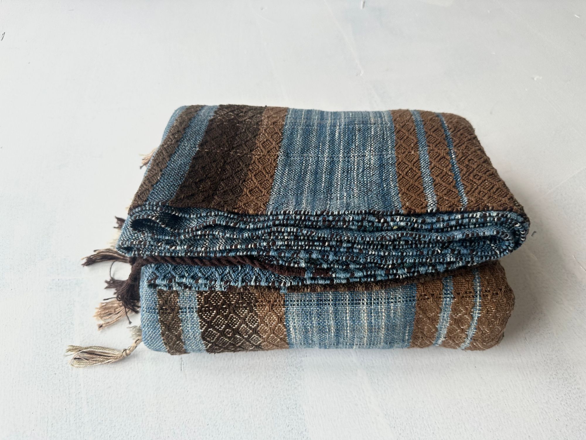 a 4.6 meter piece of handwoven fabric that is indigo blue and deep walnut dyed brown lays on a white floor