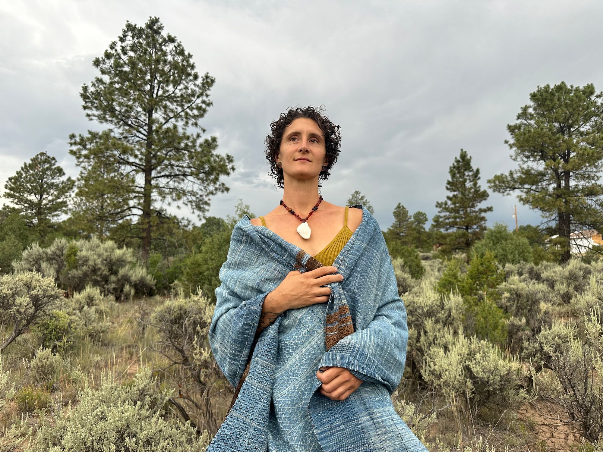 a 4.6 meter piece of handwoven fabric that is indigo blue and deep walnut dyed brown wrapped around the shoulders of a woman wearing an amber necklace